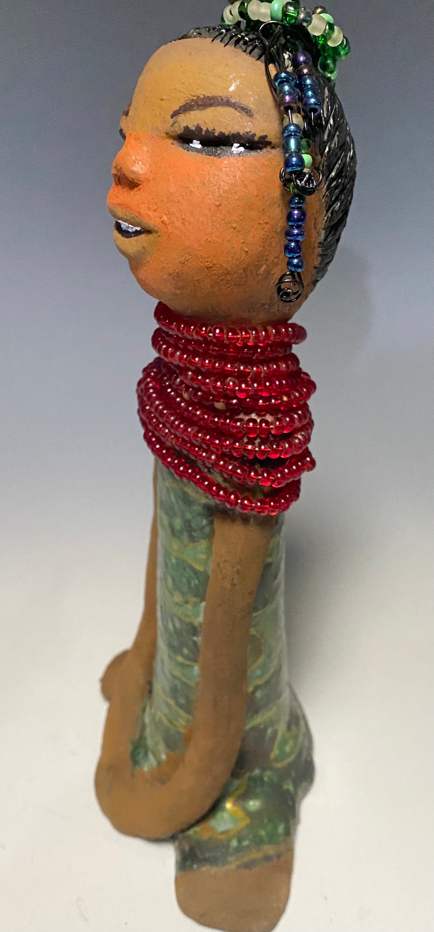 Meet Julia! Julia stands 10" x 6" x 5" and weighs 1.10 lbs. She has a lovely two tone honey brown complexion. Julia black etched hair has two beaded braids! Julia has a metallic antique copper green glazed dress. With her eyes opened and her long arms at her side, she has something to say! " I am just waiting on you to invite me into your home!" Julia will place a smile on your face and spark interesting conversation!