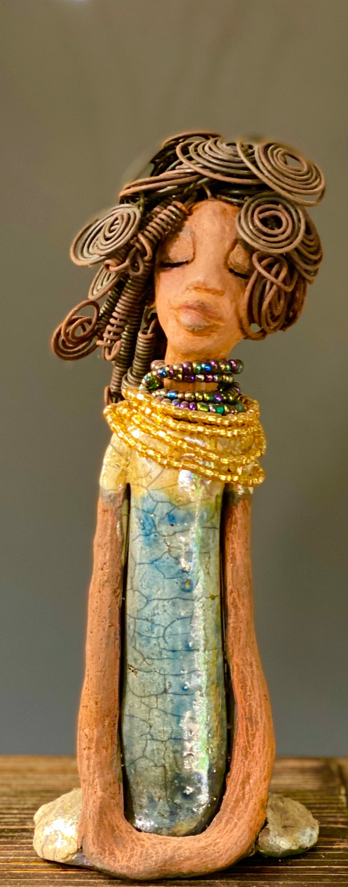 Sophia knows but will never tell! Sophia stands 10.5" x 4" x 3" and weighs 1.10 lbs. She has a honey brown complexion with curls, coils and twisted, wire hair. Sophia wears a light blue crackle dress with a dazzling gold and multicolored beaded necklace. Yes, Sophia knows something but she will never tell. Sophia will spark a conversation of "say what" in your place.