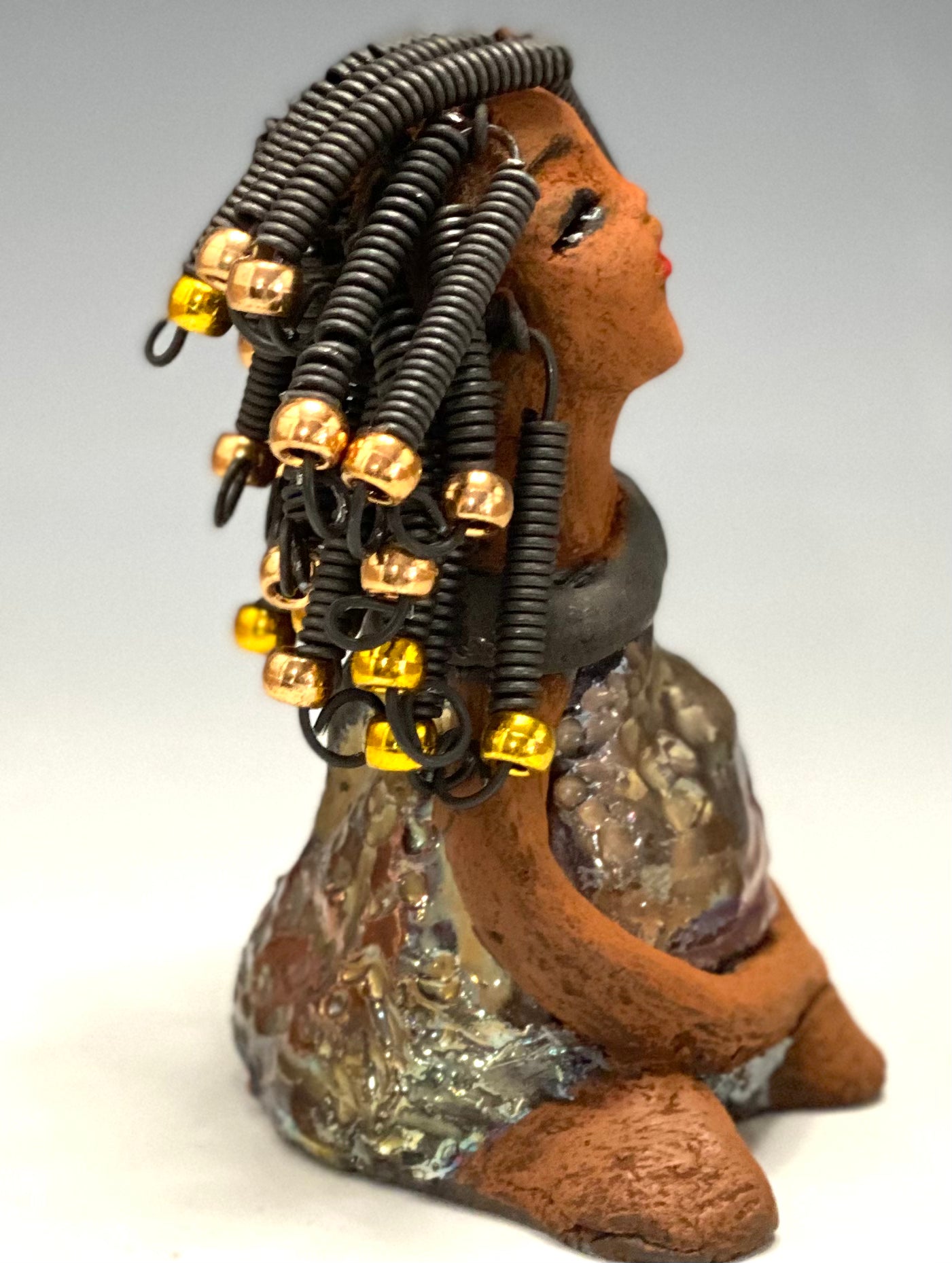 Meet Sadie Sadie stands 5.5" x 4" x 3" and weighs 8.7 ozs. She wears a lovely glossy metallic gold dress.. Sadie has over15 feet of coiled wire hair. Sadie appears to sit in a yoga pose. Her long arms rest at her side. Sadie is a great starter piece from the Herdew Collection!
