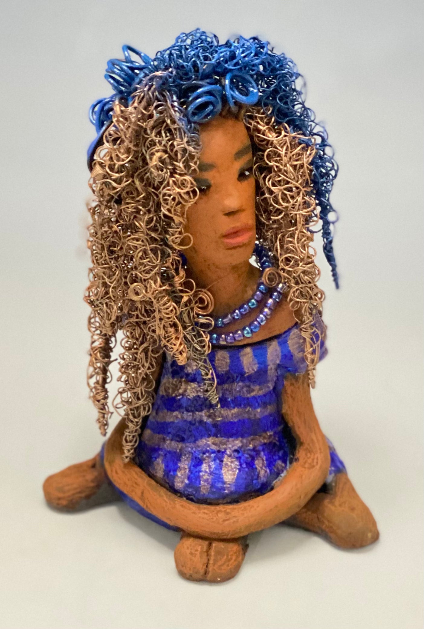 Sherrie stands 6" x 4" x 4.5" and weighs 12.6 ozs. She has a lovely honey brown complexion with reddish brown lips. Sherrie's hairstyle is made up of over 75 feet of twisted 24 gauge wire. Sherrie has a striped metallic copper and blue glazed dress. She wears a aqua blue beaded necklaces. With eyes wide opened, Sherrie has hope of finding a new home. She will make an excellent starter piece from the HerDew collection!