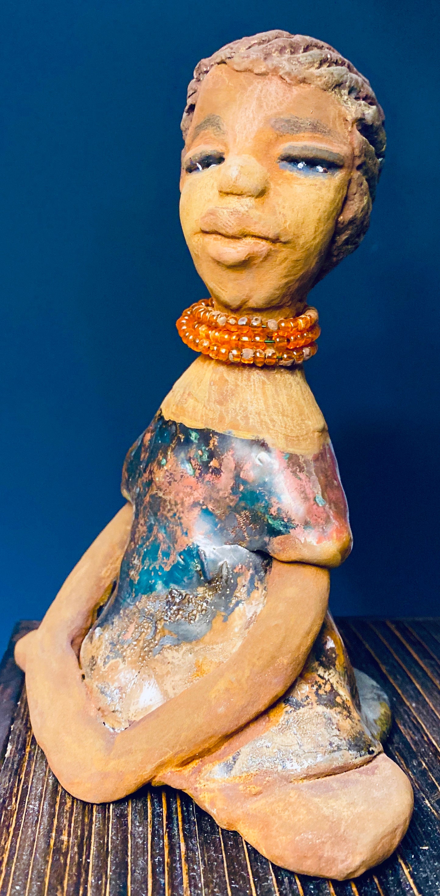 Meet Devonte! Devonte stands 8" x 6" x 4" and weighs 1.06 lbs. Devonte has a awesome honey brown complexion. She has braided clay hair. Devonte has long loving arms. She wears a metallic copper dress with red orange beads. Give Devonte a special place in your home!