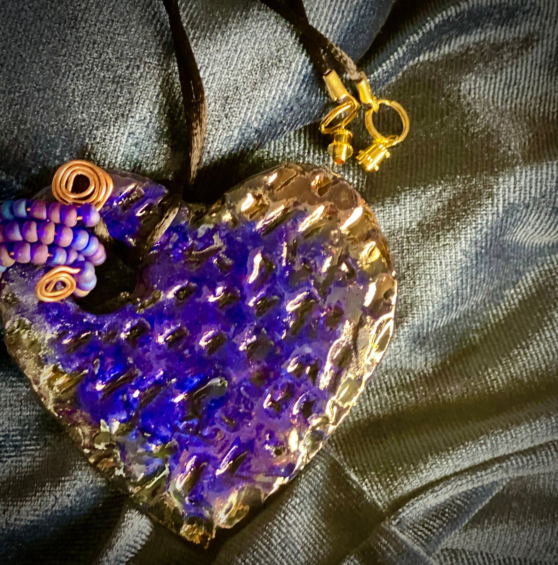 Have A Heart ! Each heart pendant is handmade with love! It is 3"x 3" and weighs approx. 3ozs. This pendant has a royal blue and gold metallic raku glazes that renders a unique translucent  patina. The heart  has a textured  pattern. It holds a spiral of off blue violet mini beads on a spiral copper wire. This pendant has a nice 12" black suede cord!