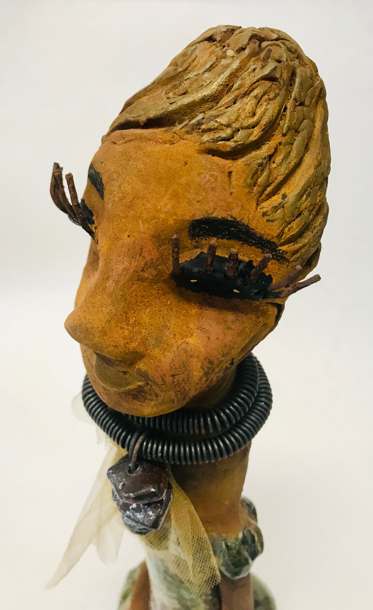 Trinity stands 14" x 4" x 4" and weighs 2.7 lbs. She has a lovely honey brown complexion with reddish brown lips. She has a braided hairstyle. Trinity has a colorful metallic green antique copper glazed dress. She wears a spiral wire necklaces with raku beads underneath an antique gold tulle.. With long lashes and eyes wide opened, Trinity has hopes of finding a new home.