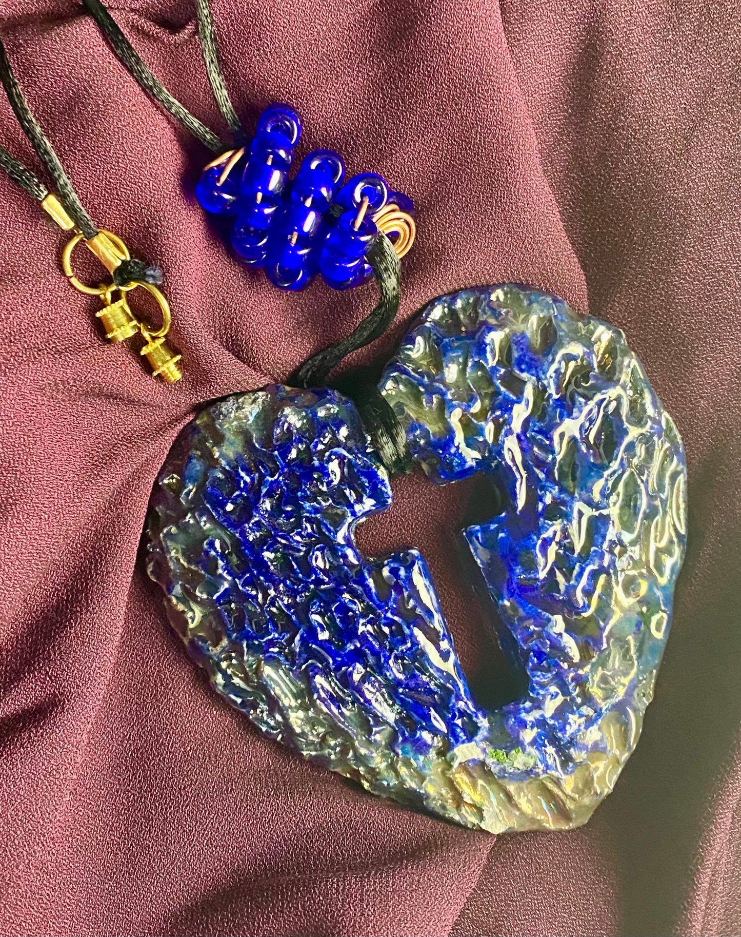 Have A Heart ! Each heart pendant is handmade with love! It is 3"x 3" and weighs approx. 3ozs. This pendant has a royal blue and gold metallic raku glazes that renders a unique translucent patina. The heart has a cut out cross in the center with a textured pattern. It holds a spiral of royal blue mini beads on a spiral copper wire. This pendant has a nice 12" black suede cord!