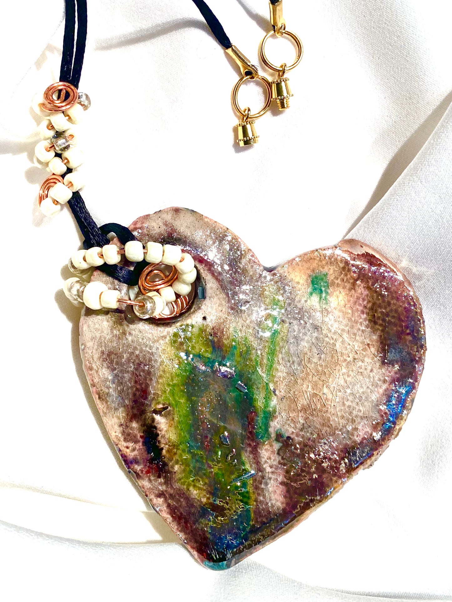 Have A Heart! Each heart pendant is handmade with love! It is 3"x 3" and weighs approx. 3ozs. This pendant has a copper gold metallic raku glazes that renders a unique translucent patina. The heart has a textured pattern . It holds a spiral of white mini beads on a spiral copper wire. This pendant has a nice 12"black rattail cord!