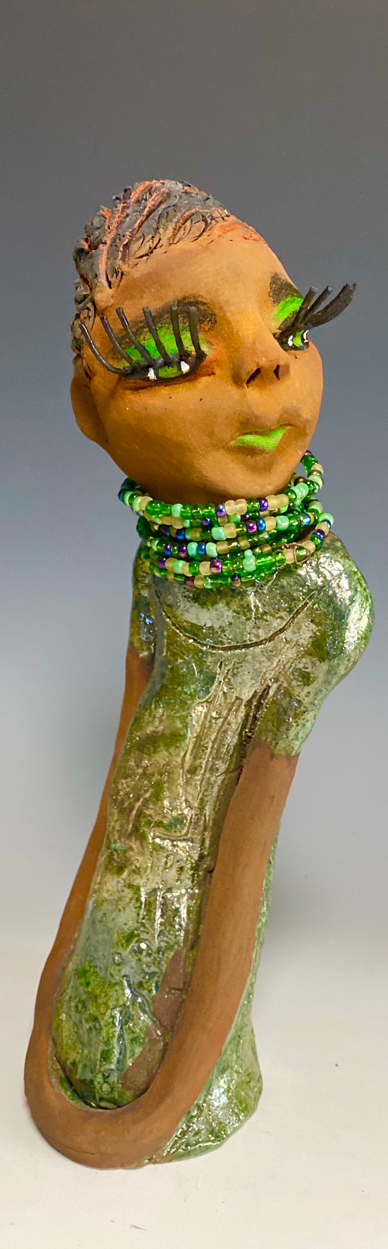 Meet Marissa! Marissa stands 11.5" x 3" x 3.5" and weighs 2.5 lbs. She has a lovely honey brown complexion with reddish brown lips. She has a braided short black clay hairstyle.  Marissa has a colorful metallic copper green antique glazed dress. She wears the world's longest eyelashes. With  her green eyes slightly opened, Marissa has hope of finding her way into your home.