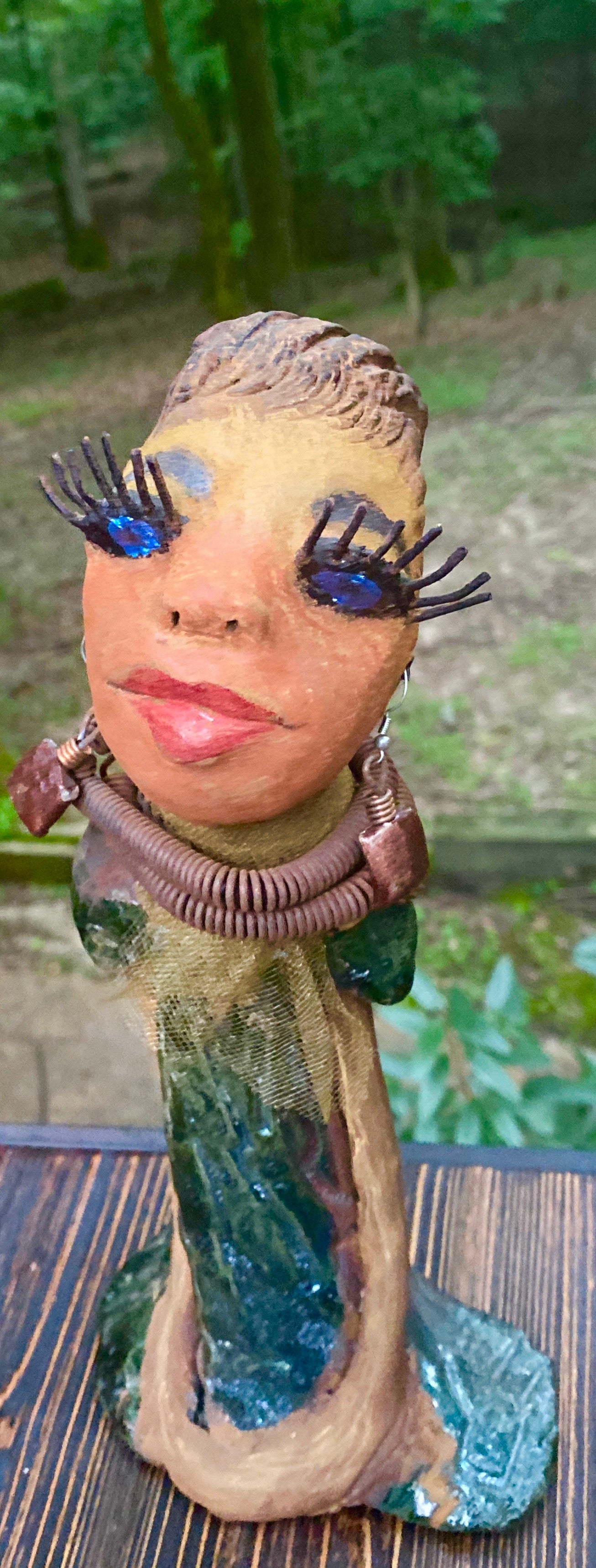 Meet Catera! Catera stands 10" x 4" x 4" and weighs 2.7 lbs. She has a lovely honey brown complexion with  reddish brown lips. She has a braided hairstyle.  Catera has a colorful metallic green antique copper glazed dress. She wears a yellow bead necklace with raku beads. Her long loving arms are resting at her side. With long lashes and eyes wide opened, Catera has hopes of finding a new home.