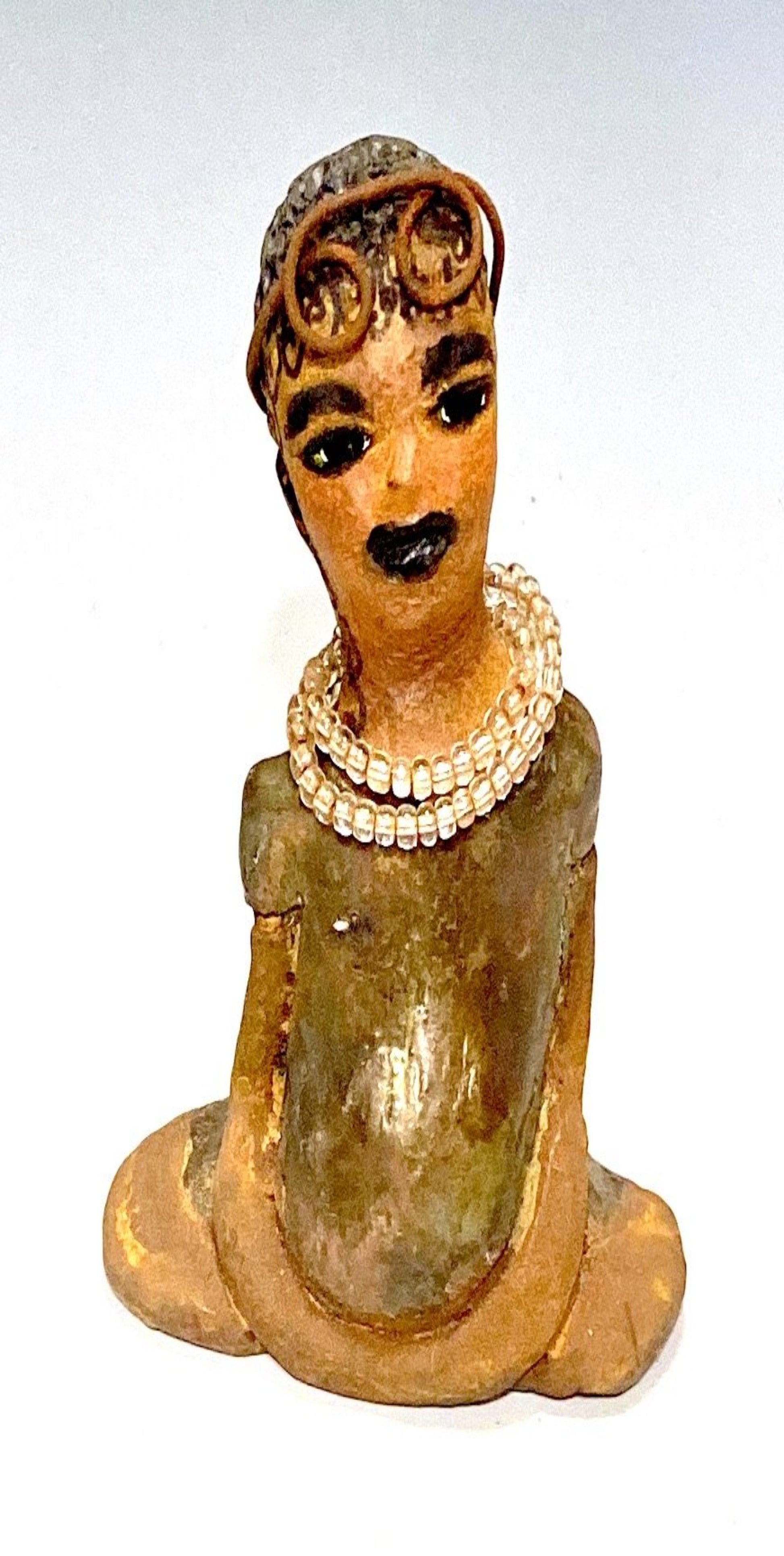 Meet karisha! Karisha stands 6" x 4" x 3" and weighs 8.7 ozs.  Karisha has a lovely glossy green dress with a matching hat.  She has curly wire hair.  Karisha appears to sit in a yoga pose. Her long arms rest at her side. Karisha is a great starter piece from the Herdew Collection!