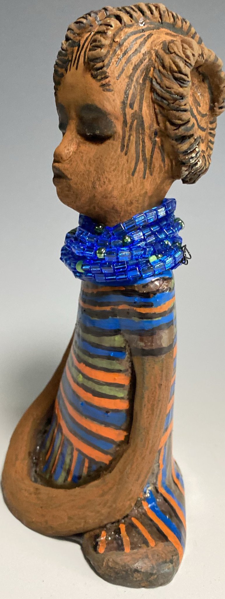 Meet Meet Harmony! Harmony stands 8' x 5"x 2" and weighs 1.7 lb. She has a nice honey brown complexion. Harmony  has stylized clay hair.  Her long trademark arms rest at her side. Harmony's dress is  colorful with  geometric flare.. She accents with a aqua blue beaded necklace. Harmony is priced right to be accepted into  your home!