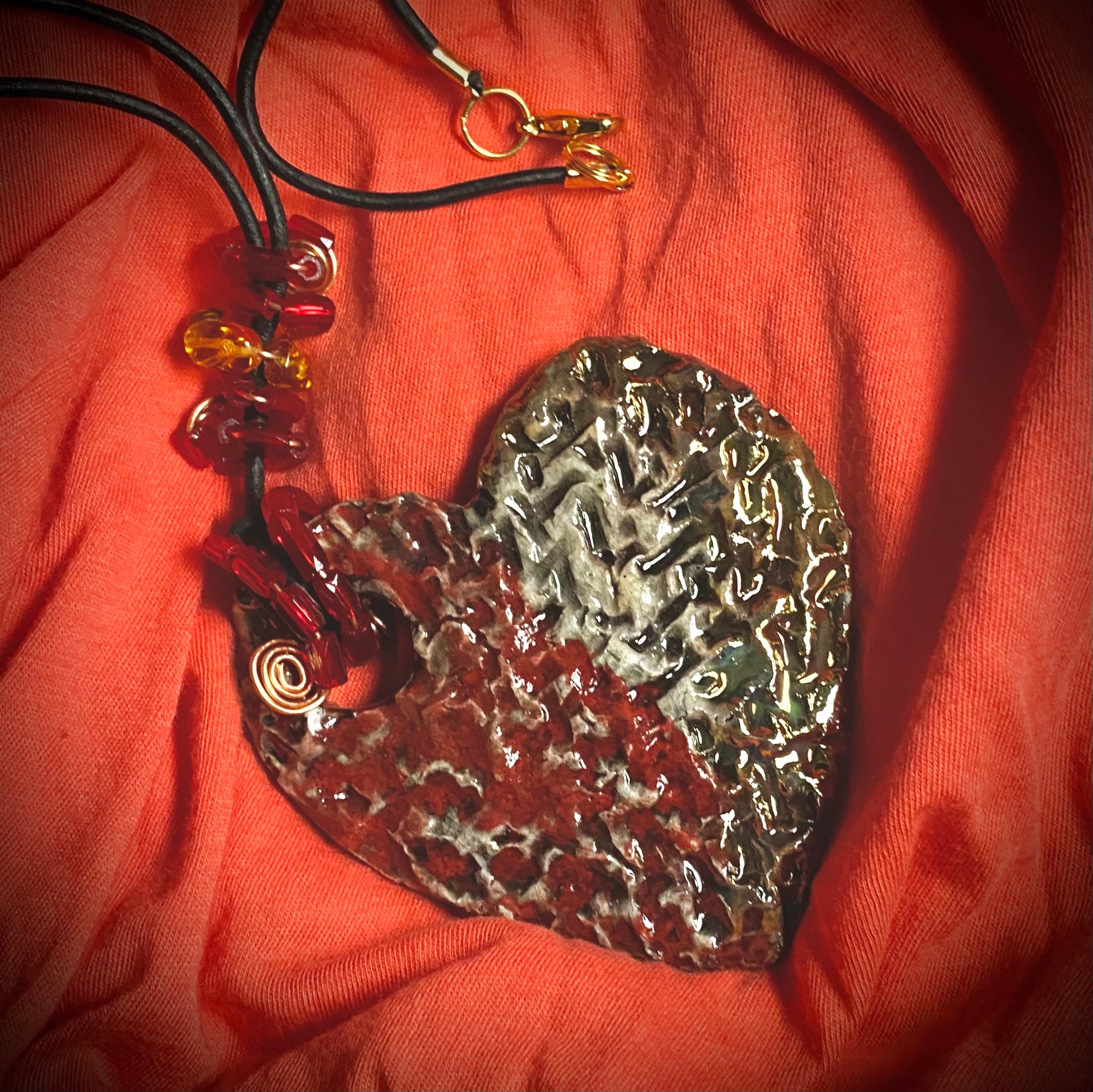 Have A Heart ! Each heart pendant is handmade with love! It is 3"x 3" and weighs approx. 3ozs. This pendant has a  ruby red and off white metallic raku glazes that renders a unique translucent  patina. The heart  has a textured  pattern. It holds a spiral of ruby red mini beads on a spiral copper wire. This pendant has a nice 12" black suede cord!