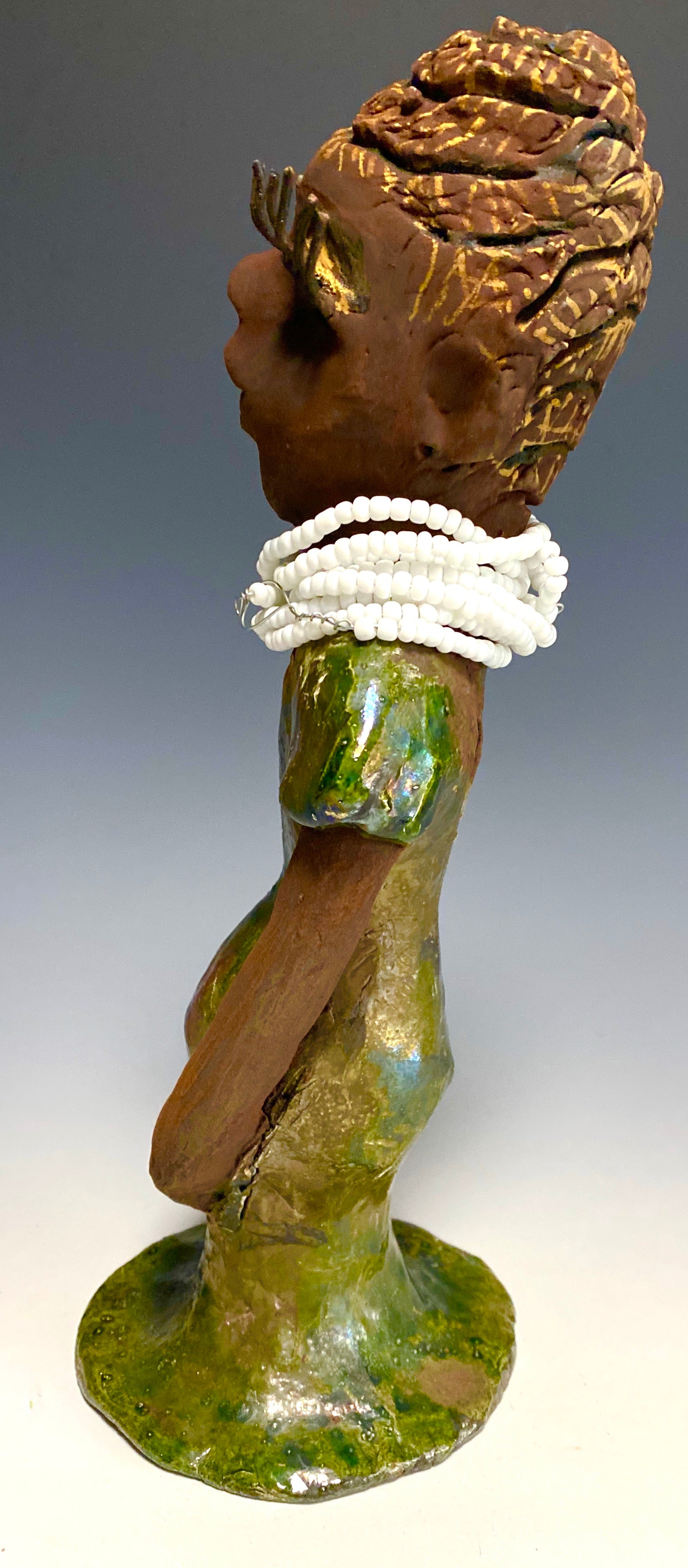 Meet Erma! Erma stands 11.5" x 5" x 5" and weighs 2 lbs. She has a lovely dark brown complexion with brown lips. She has a braided hairstyle.  Erma has a colorful metallic green antique copper glazed dress. She wears a bright white beaded necklace. With long lashes and eyes wide opened and ultra white teeth, Erma has hopes of finding her way into your home!