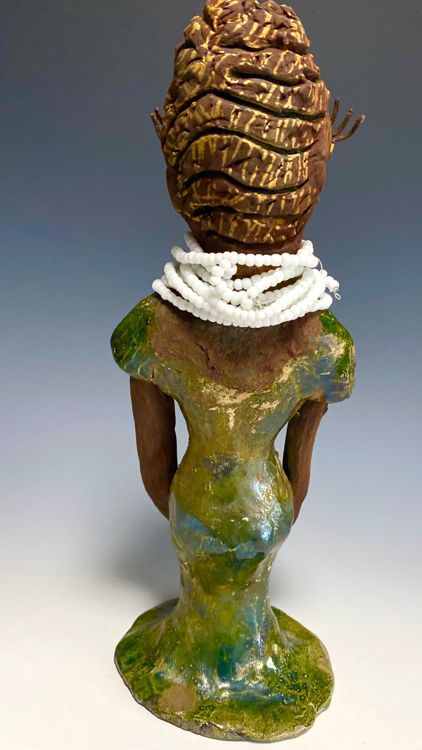 Meet Erma! Erma stands 11.5" x 5" x 5" and weighs 2 lbs. She has a lovely dark brown complexion with brown lips. She has a braided hairstyle. Erma has a colorful metallic green antique copper glazed dress. She wears a bright white beaded necklace. With long lashes and eyes wide opened and ultra white teeth, Erma has hopes of finding her way into your home!