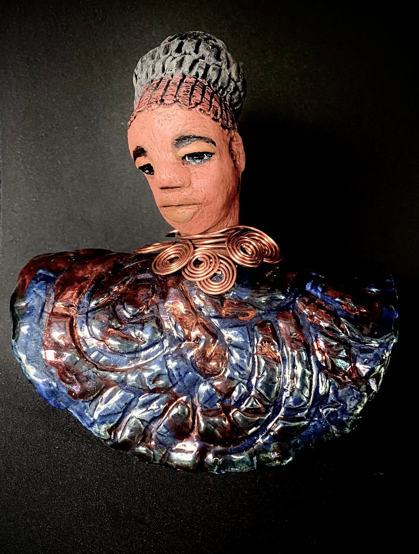 Meet Tia! Tia looks up with joy and anticipation! Tia stands 7" x 6" x 4" and weighs 1.90 lbs. She has a beautiful textured copper and blue robe. Tia has braided clay hair up in a bun. She has a honey brown complexion and soft light brown lips. Tia will make for great conversation in your home. Free Shipping! Check out our Shipping and Return policy