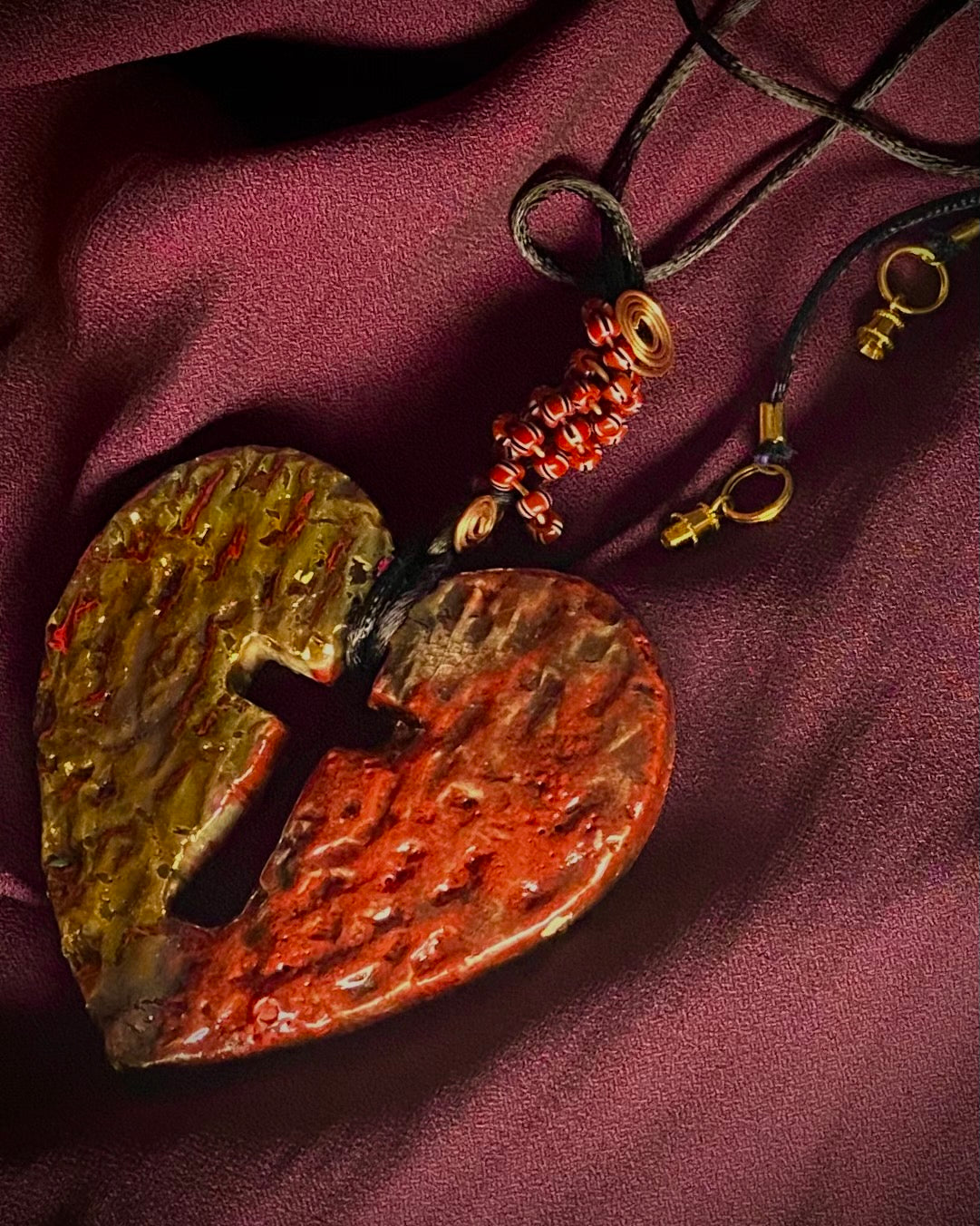 Have A Heart ! Each heart pendant is handmade with love! It is 3"x 3" and weighs approx. 3ozs. This pendant has a red and gold metallic raku glazes that renders a unique translucent patina. The heart is textured and has a cut out cross in the center. It holds a spiral of red and white mini beads on a spiral copper wire. This pendant has a nice 12" black suede cord!