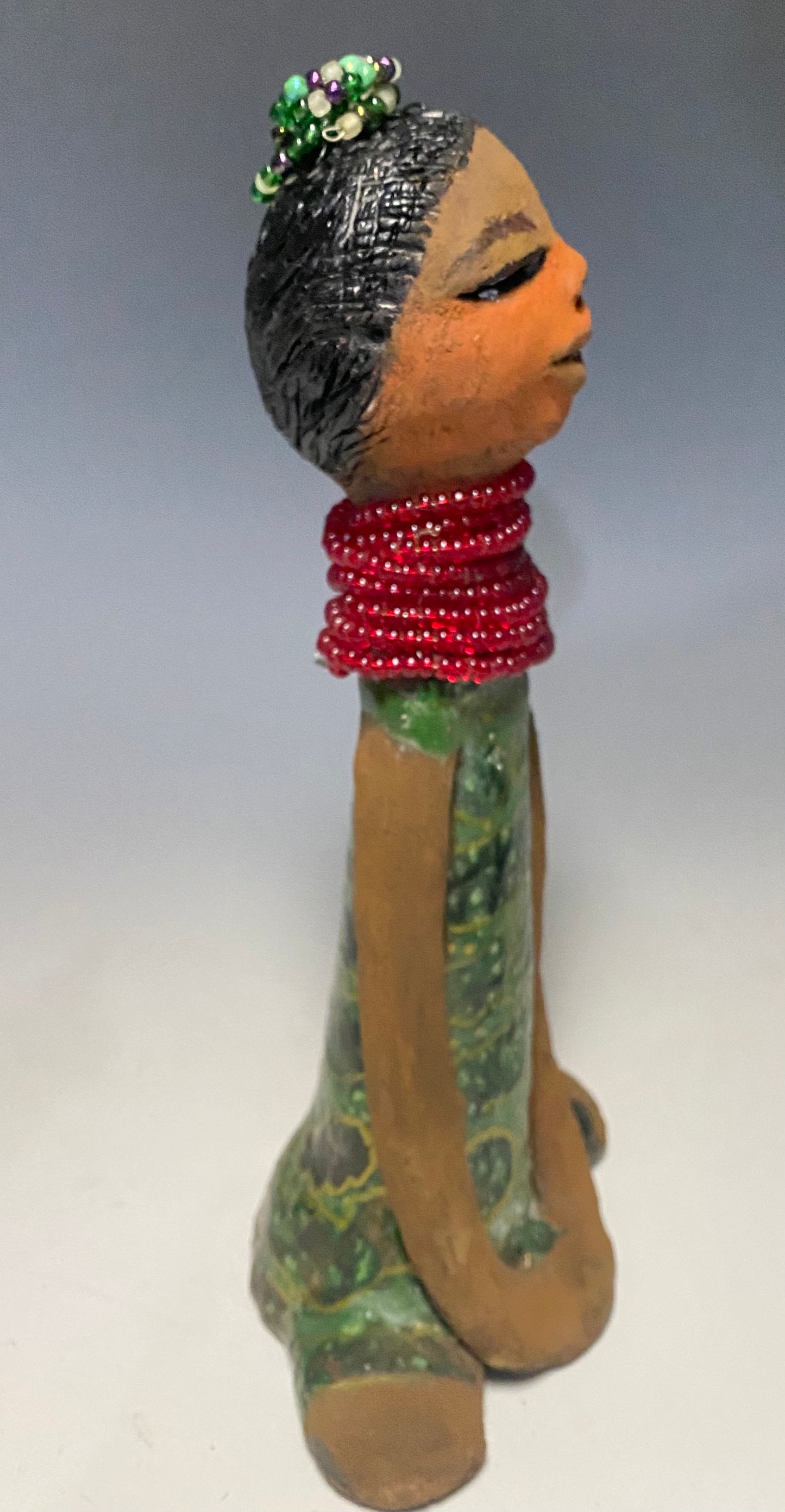 Meet Julia! Julia stands 10" x 6" x 5" and weighs 1.10 lbs. She has a lovely two tone honey brown complexion. Julia black etched hair has two beaded braids! Julia has a metallic antique copper green glazed dress. With her eyes opened and her long arms at her side, she has something to say! " I am just waiting on you to invite me into your home!" Julia will place a smile on your face and spark interesting conversation!