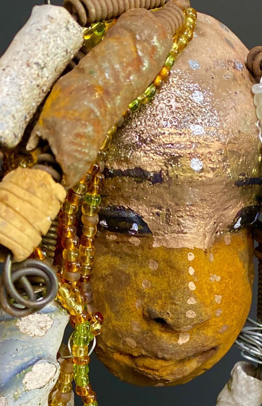 I started making art soon after seeing authentic African artwork at the Smithsonian Museum of African Art. I was in total awe. Ryanna was inspired by my visit there. Ryanna is 8”x 6” and weighs 13 ozs. She has a two tone earthy honey and metallic gold complexion. Ryanna has over 20 raku beads and over a 100 mini colored and white beads spiral coils of hair. She more than 10 feet of 16 gauge wire hair