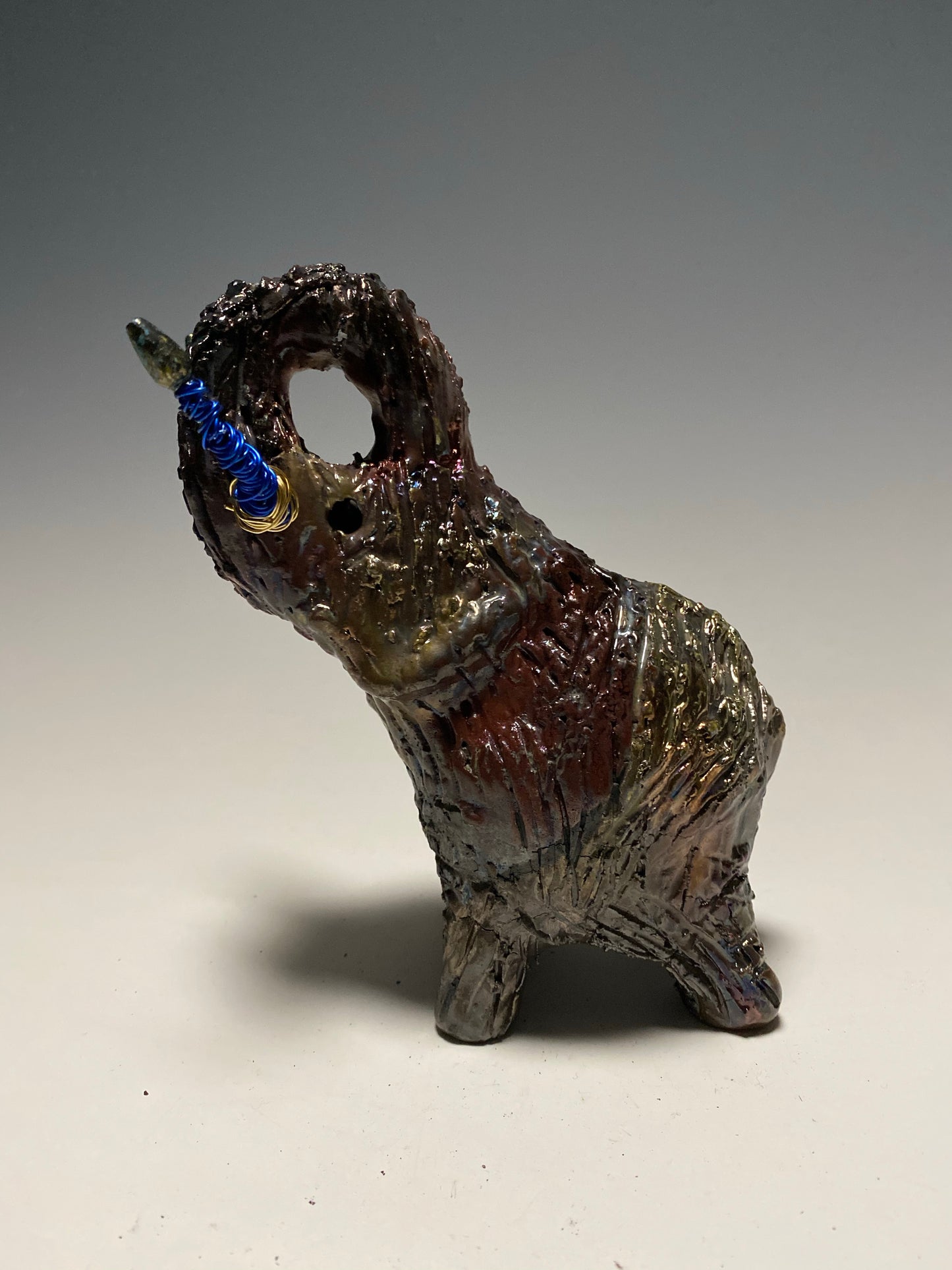 Raku Elephant Have you HERD!!!!!! Just one of these lovely Raku Fired Elephant will make an excellent gift for your friend, sorority or for your home’ special place centerpiece. 6" x 4" x 4" 1 lbs Beaded tusk with blue and gold wire Beautiful colorful metallic raku elephant For decorative purposely only