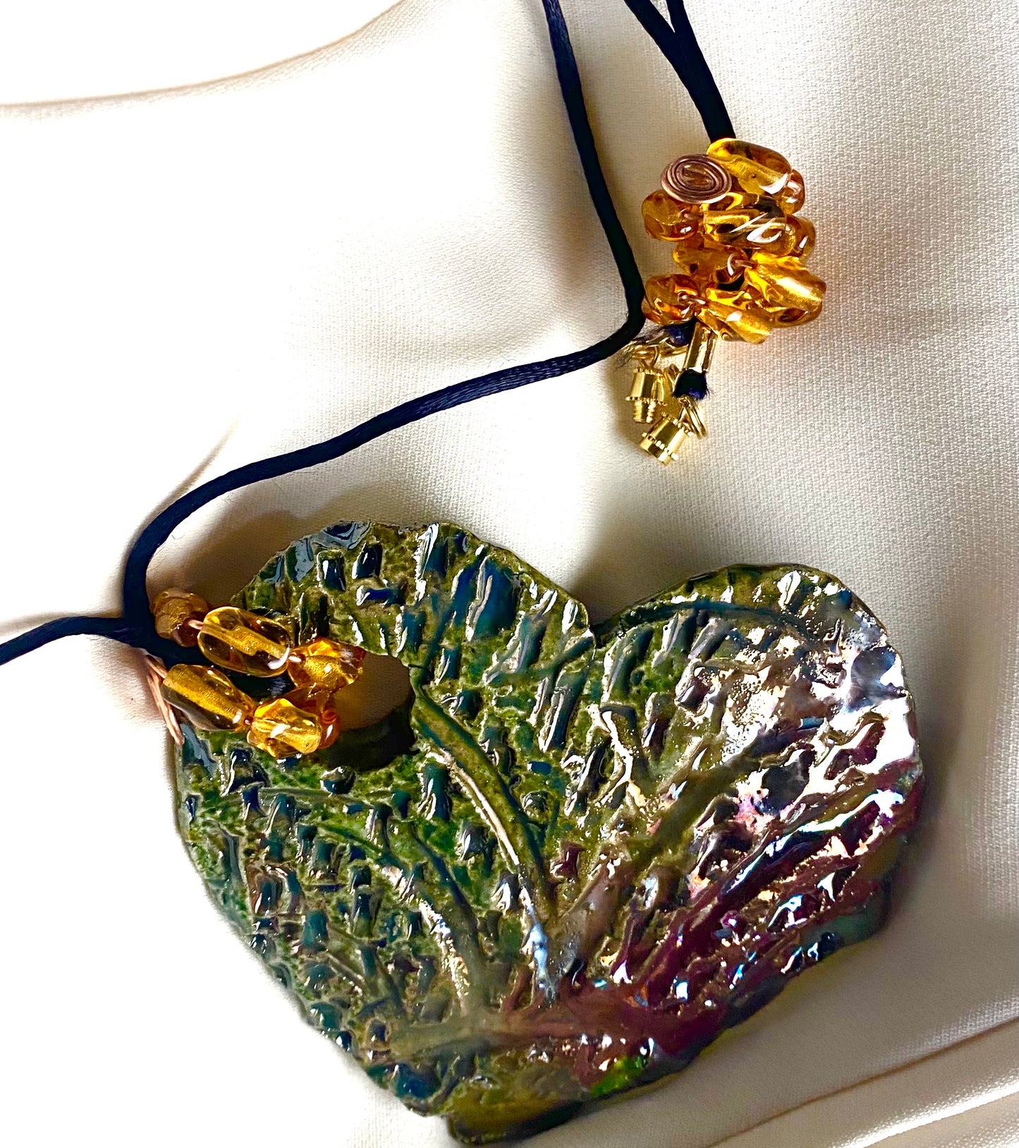 Have A Heart ! Each heart pendant is handmade with love! It is 3"x 3" and weighs approx. 3ozs. This pendant has an alligator green and gold metallic raku glazes that renders a unique translucent patina. The heart has a textured pattern. It holds a spiral of amber mini beads on a spiral copper wire. This pendant has a nice 12" black suede cord!