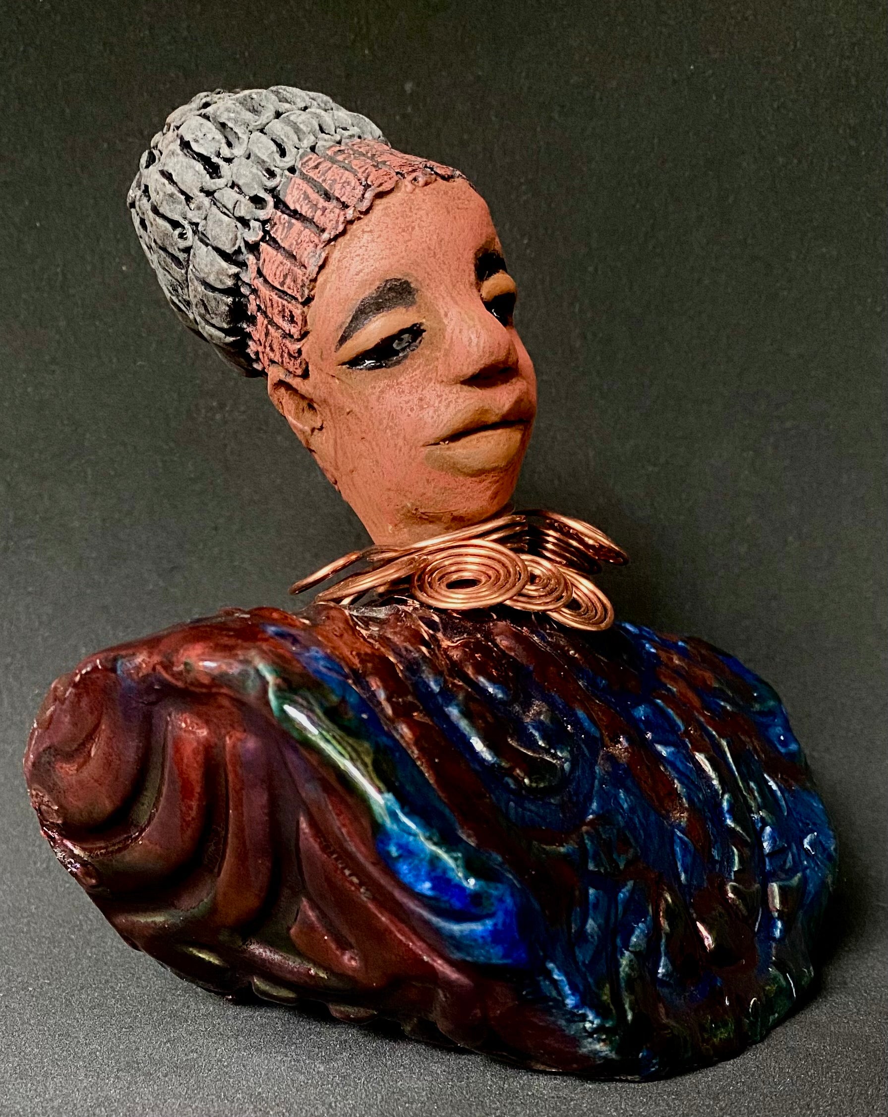 Meet Tia! Tia looks up with joy and anticipation! Tia stands 7" x 6" x 4" and weighs 1.90 lbs. She has a beautiful textured copper and blue robe. Tia has braided clay hair up in a bun. She has a honey brown complexion and soft light brown lips. Tia will make for great conversation in your home.  Free Shipping! Check out our Shipping and Return policy