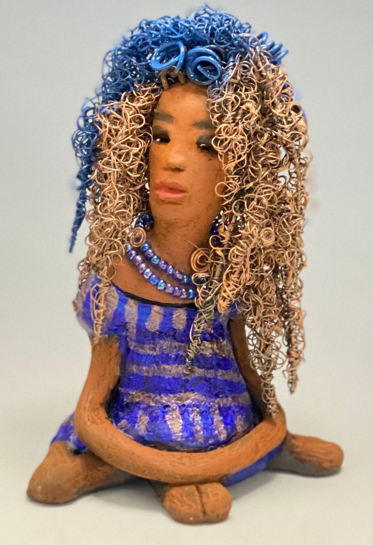 Sherrie stands 6" x 4" x 4.5" and weighs 12.6 ozs. She has a lovely honey brown complexion with reddish brown lips. Sherrie's hairstyle is made up of over 75 feet of twisted 24 gauge wire. Sherrie has a striped metallic copper and blue glazed dress. She wears a aqua blue beaded necklaces. With eyes wide opened, Sherrie has hope of finding a new home. She will make an excellent starter piece from the HerDew collection!