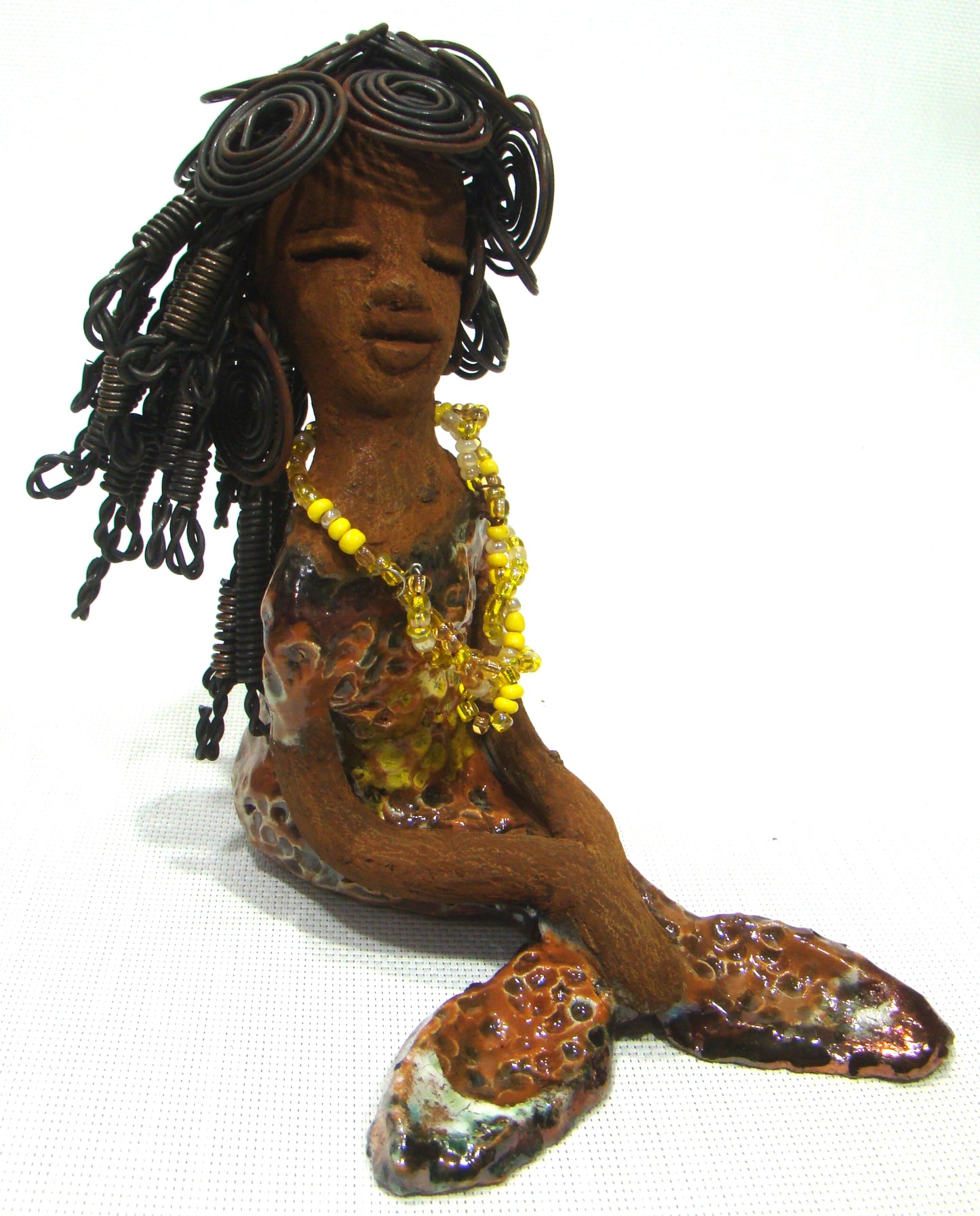 Meet Isabella the Mermaid! Isabella stands 7' x 4" x 6" and weighs 1.08 lbs.. Isabella has a lovely brown complexion. Her long loving arms are crossed in her lap. Isabella has over 20 feet of wire hair. It took over two hours to fix her hair! Isabella has a metallic yellow swimsuit with flashes of copper. She wears a yellow beaded necklace. Isabella appears to have something on her mind!
