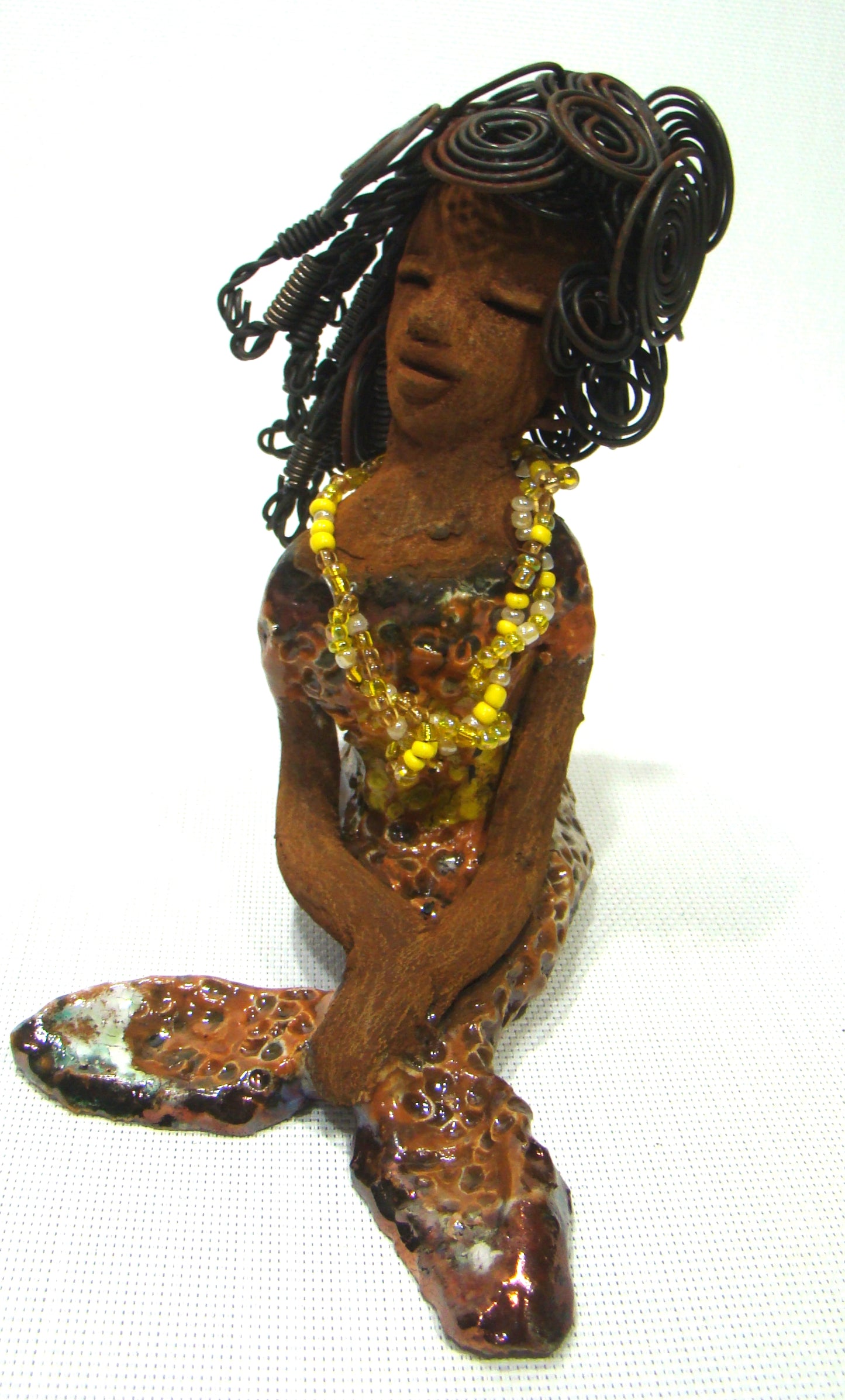 Meet Isabella the Mermaid! Isabella stands 7' x 4" x 6" and weighs 1.08 lbs.. Isabella has a lovely brown complexion. Her long loving arms are crossed in her lap. Isabella has over 20 feet of wire hair. It took over two hours to fix her hair! Isabella has a metallic yellow swimsuit with flashes of copper. She wears a yellow beaded necklace. Isabella appears to have something on her mind!