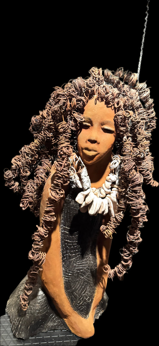 This evocative sculpture by Lester Jones celebrates the beauty, strength, and cultural heritage of African-descended women through form, texture, and symbolism. The figure’s elaborate crown of coiled wire hair evokes vitality, creativity, and a sense of reverence. Her closed eyes and serene expression suggest introspection, grace, or spiritual grounding. Adorned with a necklace clay shell-like forms and dressed in a patterned robe, the sculpture bridges ancestral tradition and modern artistry.


