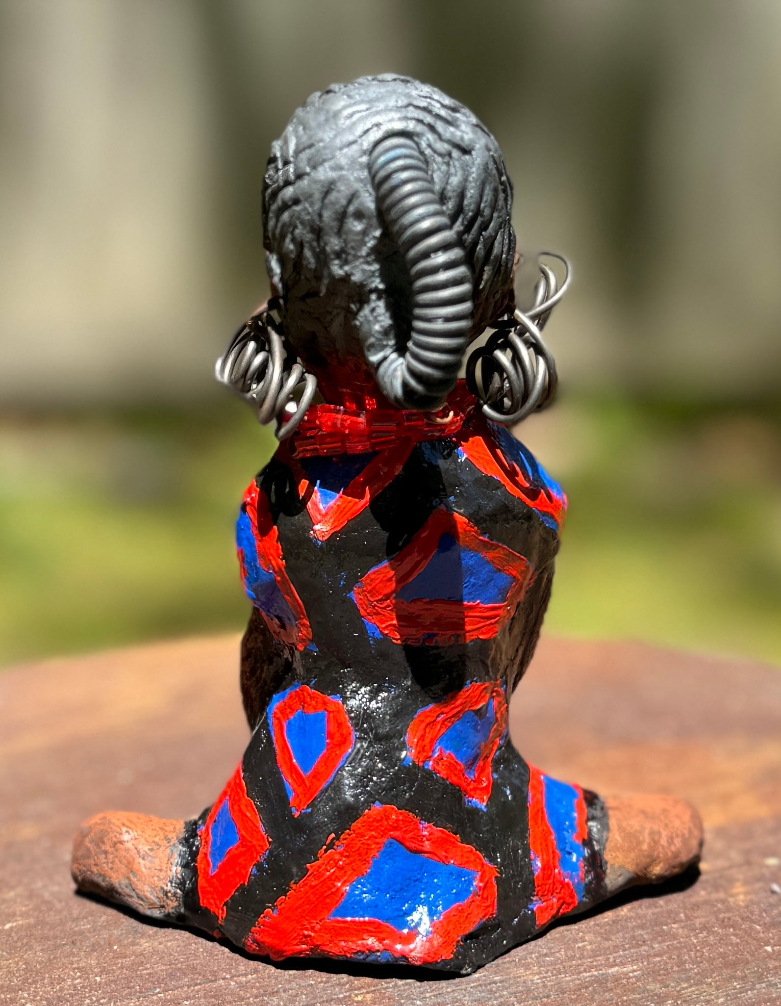 Embark on a thrilling journey with Tia from the Herdew Collection! This daring raku fired sculpture stands tall at 6" x 4" x 3" and weighs a fearless 9.6 ozs. Adorned in a striking geometric print dress, Tia's coiled wire hair stretches over 1 foot. With determined outstretched arms, she strikes a powerful yoga pose. Start your collection with the captivating Tia and embrace the thrill of adventure!