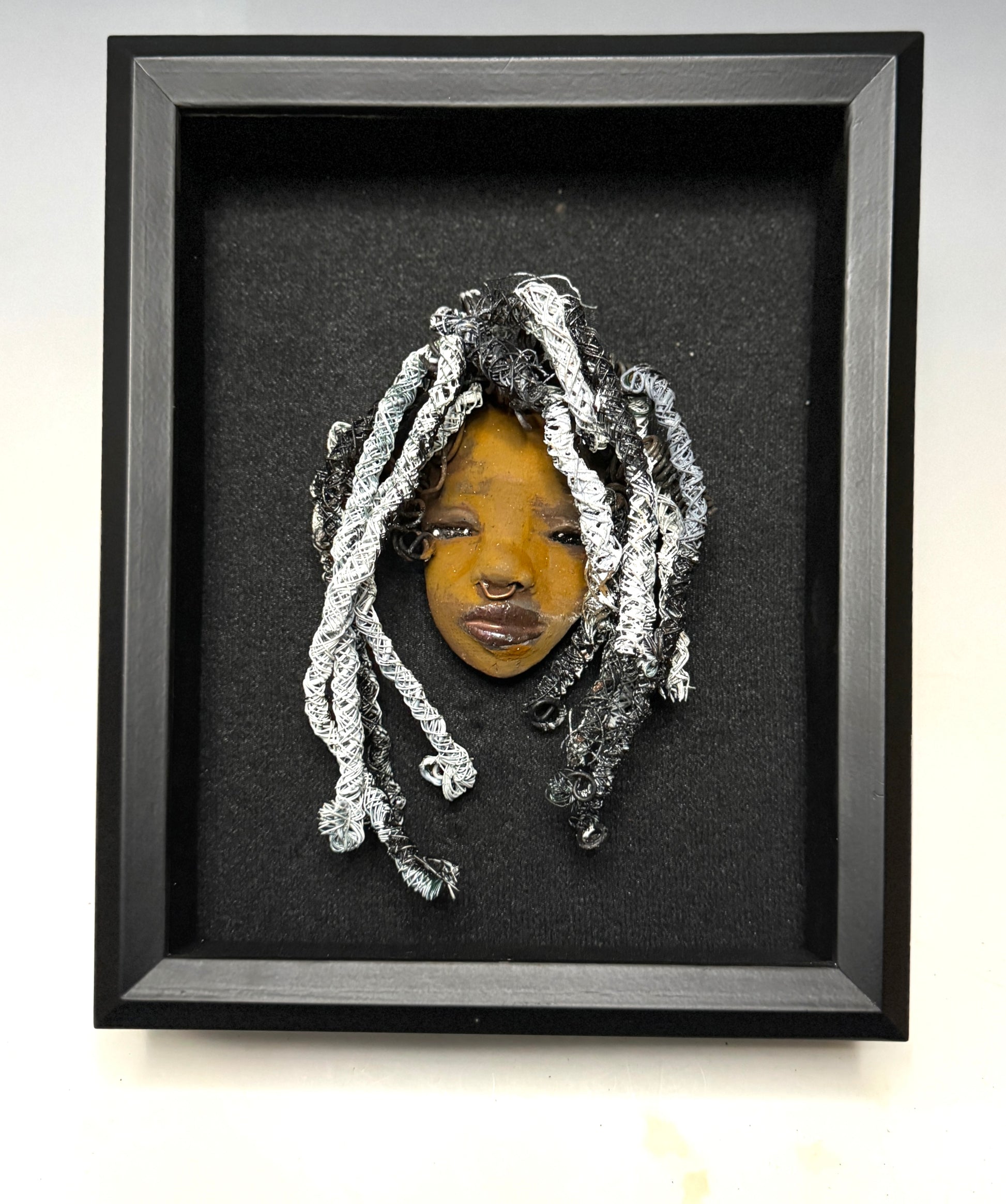 Weighing 5 oz and with a diameter of 3" by 7", Bailey Rae adds a hint of elegance to any wall, tree or shadowbox. Her black and white braids, honey brown complexion and copper-colored lips make her the perfect first piece from the HerDew mask collection. Shadow box not included with Bailey Rae purchase.