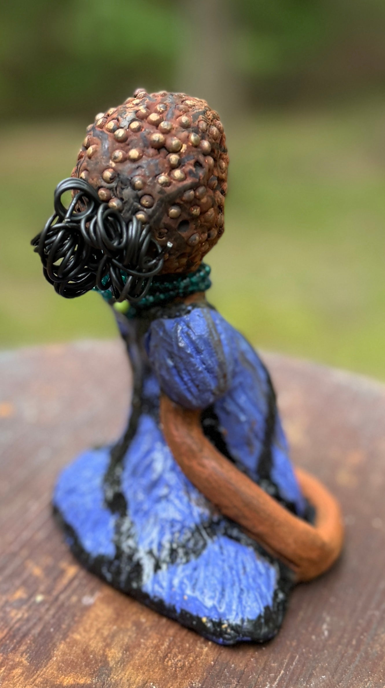 Angela is 7" x 5" x 3" raku fired sculpture and weighs 1.2 lbs.<br>She wears a lustrous African striped purple blue dress.<br>Her coiled and beaded wire hair is her crown of glory.<br><br>Angela sits in a yoga pose. Her expression is &nbsp;of curiosity. She will make an ideal beginning piece from the Herdew Collection!<br>Free Shipping