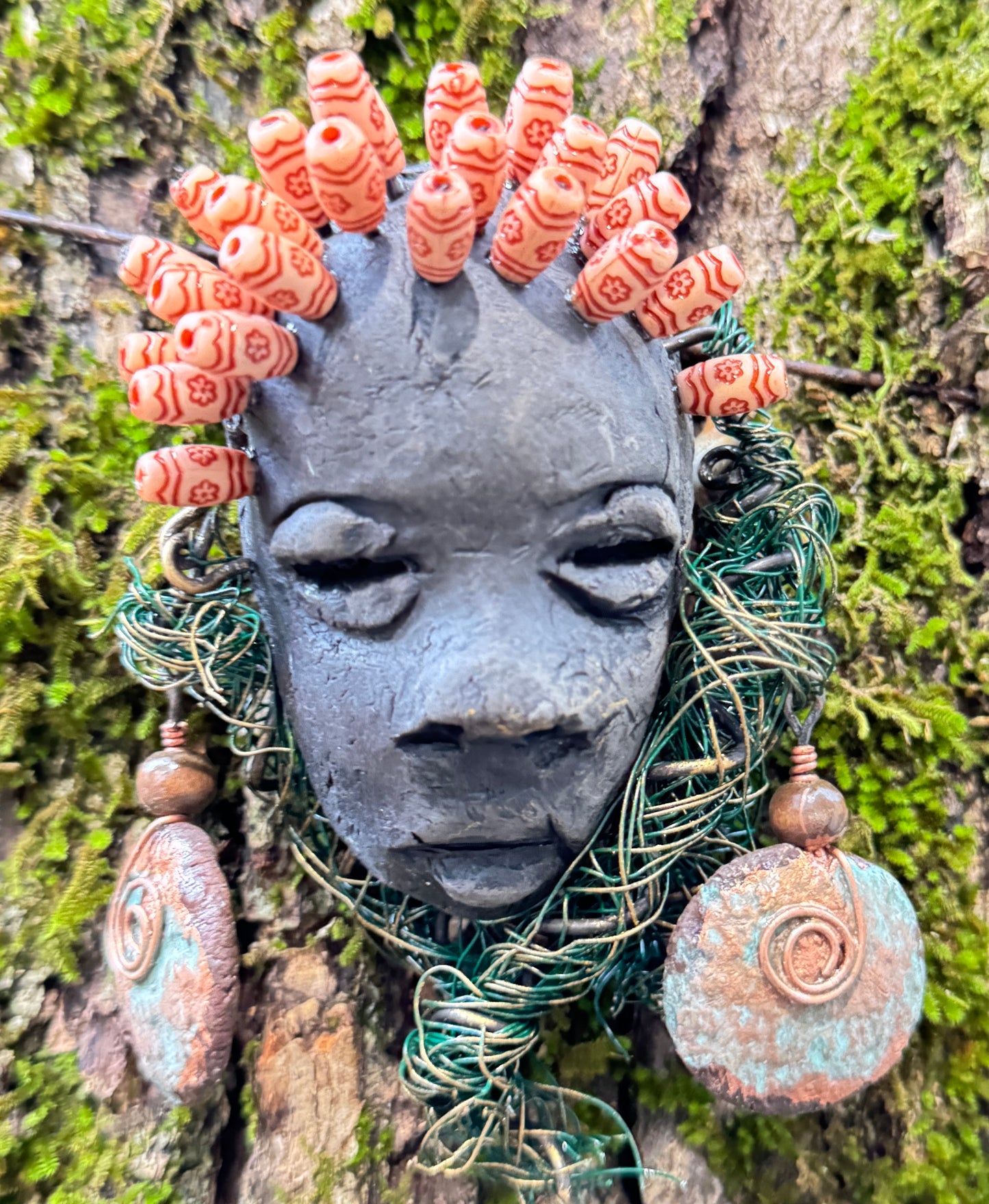 Catto is a 4” x 6” 6oz. mixed media raku fire mask made with 25 feet of 24 and 16 gauge wire. It has a stunning Smokey black complexion and comes with a large Raku fired earring and a wooden bead headdress. This makes Catto a lovely addition to your HerDew mask collection.