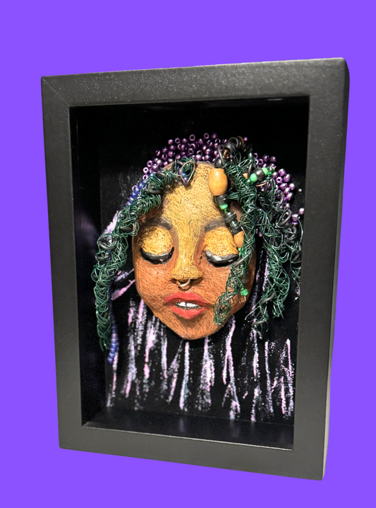 Kenti is a 5"x 7" raku mask displayed in a glass covered black shadowbox, accented with a beautiful two-tone honey brown complexion. Her intricate hair, made of 16 and 24 gauge wire and beads measures over 50 feet in length. With a contagious smile, Kenti adds a touch of elegance to any home decor.