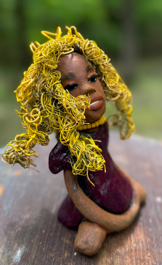 Kerri measures 6" x 4" x 3" and weighs 14ozs. She dons a stunning ruby red dress, her coiled yellow wire hair serving as her crown of glory. Poised in a yoga pose, her expression reflects curiosity. She is the perfect addition to the Herdew Collection, embodying adventure and risk-taking! Enjoy free shipping and check out our return policy.