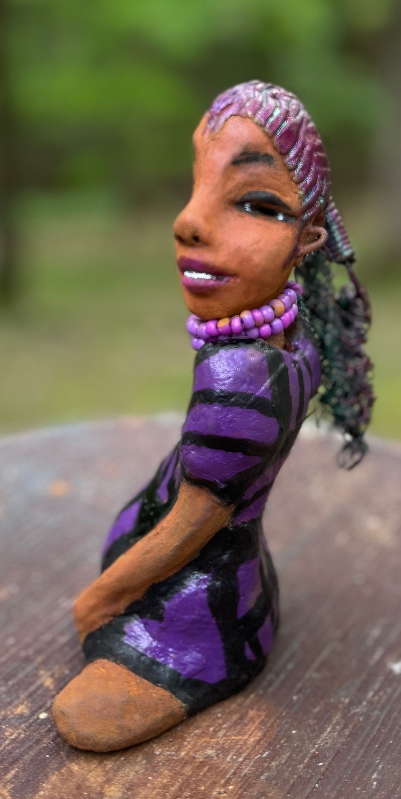 Zola is 7" x 5" x 3" raku fired scupture and weighs 12 ozs.<br>She wears a lustrous striped purple dress.<br>Her coiled wire hair is her crown of glory.<br><br>Zola sits in a yoga pose. Her expression is &nbsp;of curiosity. She will make an ideal beginning piece from the Herdew Collection!<br>Free Shipping