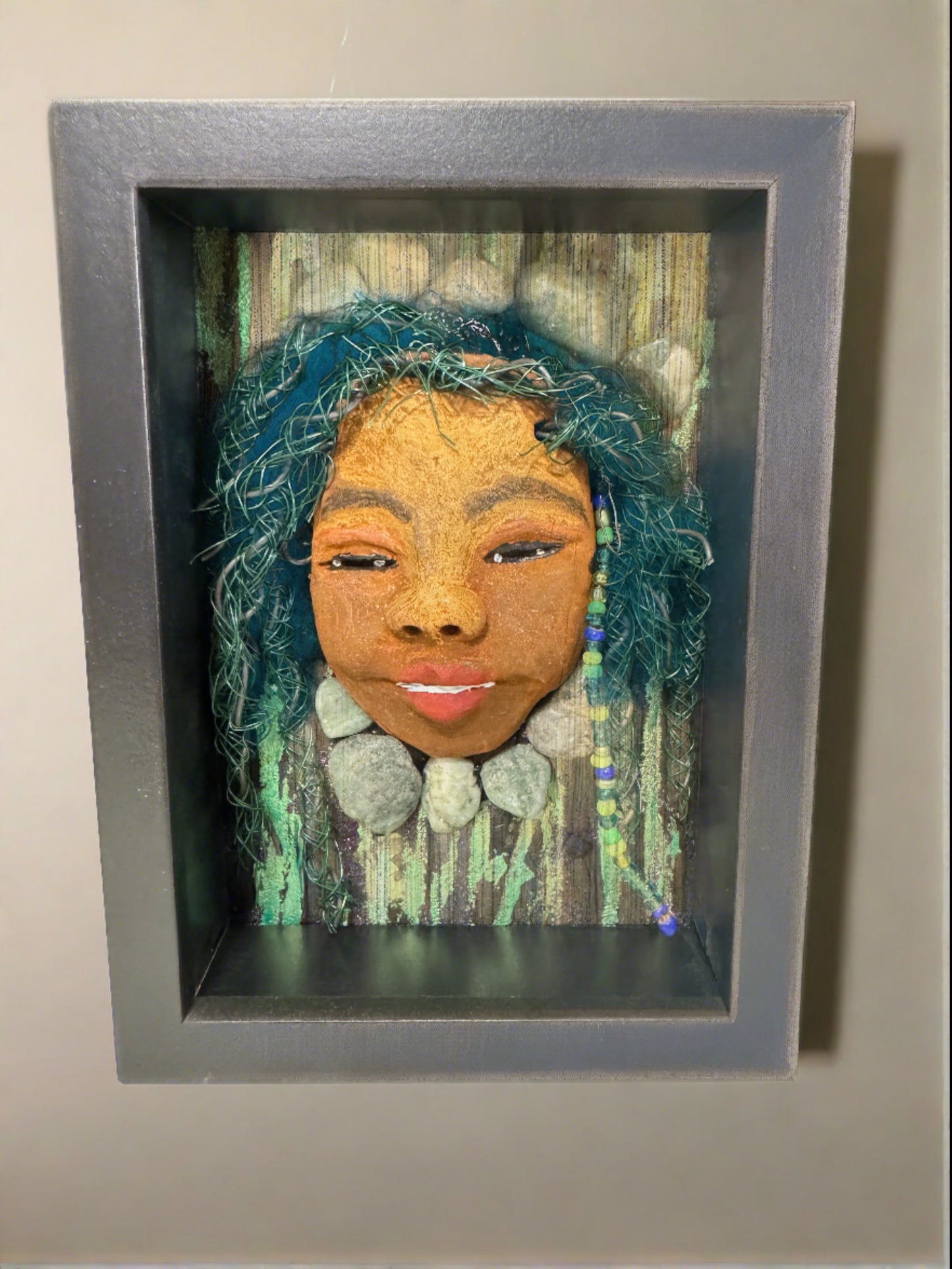 Introducing Allie, a mixed media sculpture raku fired mask. Her features include a two-tone honey brown complexion, Ruby red lips, and hair intricately intertwined with 16 and 24 gauge wire. She is mounted on a hand-painted canvas, accented by  landscaped background, and enclosed in a 5“ x 7“ black shadowbox.