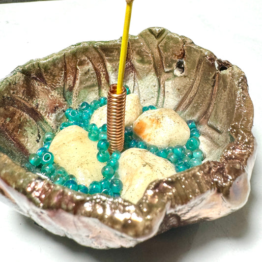 This 1" x 3" x 3" incense holder has been expertly crafted with earthy off-white stones and aqua blue beads and coated in a copper high gloss Raku glaze.