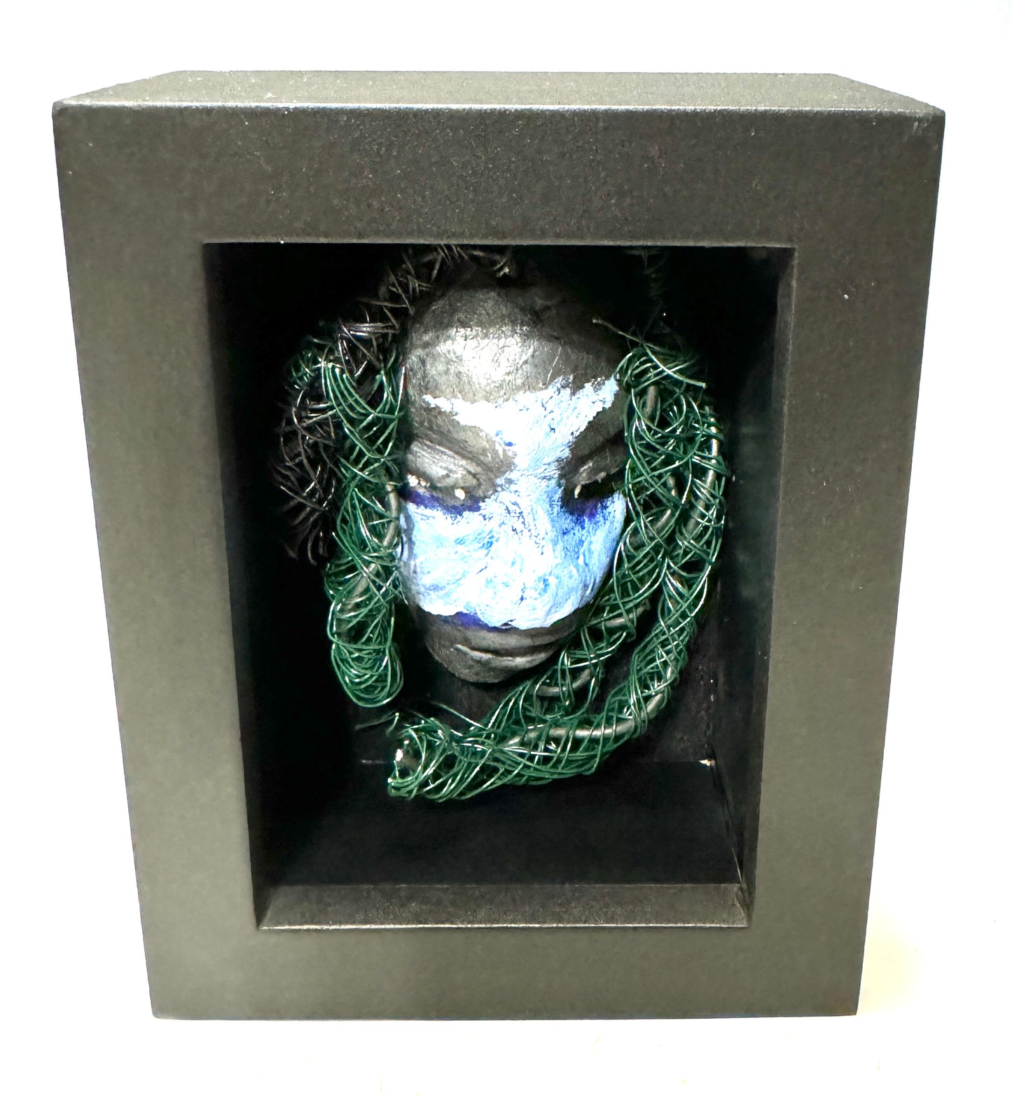 Chandon is a raku fired mask .He is enclosed in a 4“ x 4“ glass covered black shadowbox. He has over 40 feet of 16 and 24 gauge wire as hair. Make a bold statement with this striking mask! Enclosed in a sleek glass shadowbox, Chandon features a unique raku firing technique that makes each creation one-of-a-kind. The wire "hair" extends over 40 feet in length, representing a spirit that is free to explore and take risks. Bring a touch of adventure into your home with this handcrafted piece.