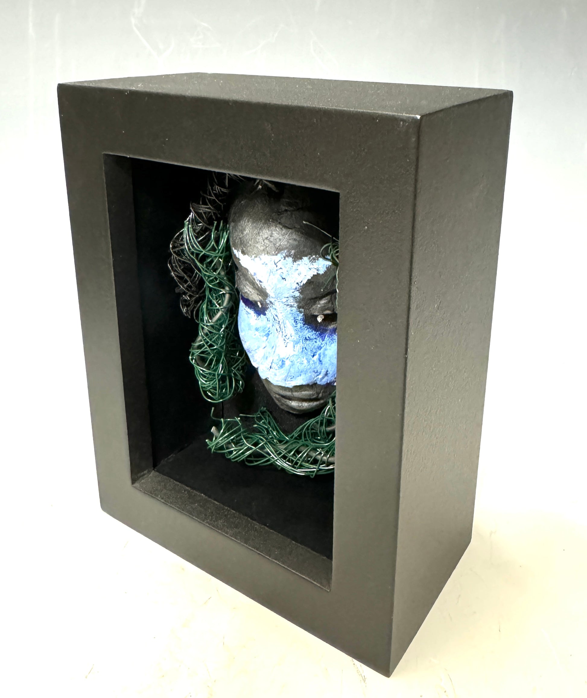 Chandon is a raku fired mask .He is enclosed in a 4“ x 4“ glass covered black shadowbox. He has over 40 feet of 16 and 24 gauge wire as hair. Make a bold statement with this striking mask! Enclosed in a sleek glass shadowbox, Chandon features a unique raku firing technique that makes each creation one-of-a-kind. The wire "hair" extends over 40 feet in length, representing a spirit that is free to explore and take risks. Bring a touch of adventure into your home with this handcrafted piece.