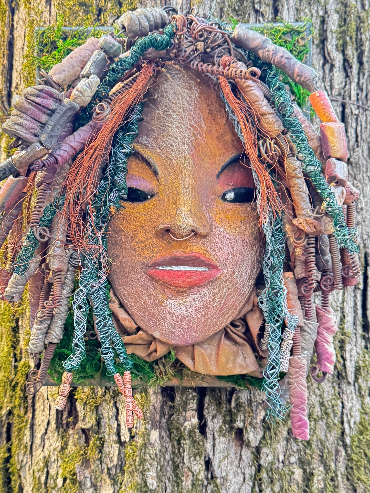 Uncover the magnificent charm of Dallas, a handcrafted raku fire mask embellished with over 60 beads and made using 24, 16 gauge wire and various mixed media. This exceptional creation has a weight of approximately 3 pounds and is attached to a 10” x 12" canvas. The natural two tone face and braided, beaded hair make it a distinctive addition to your indoor or outdoor design.