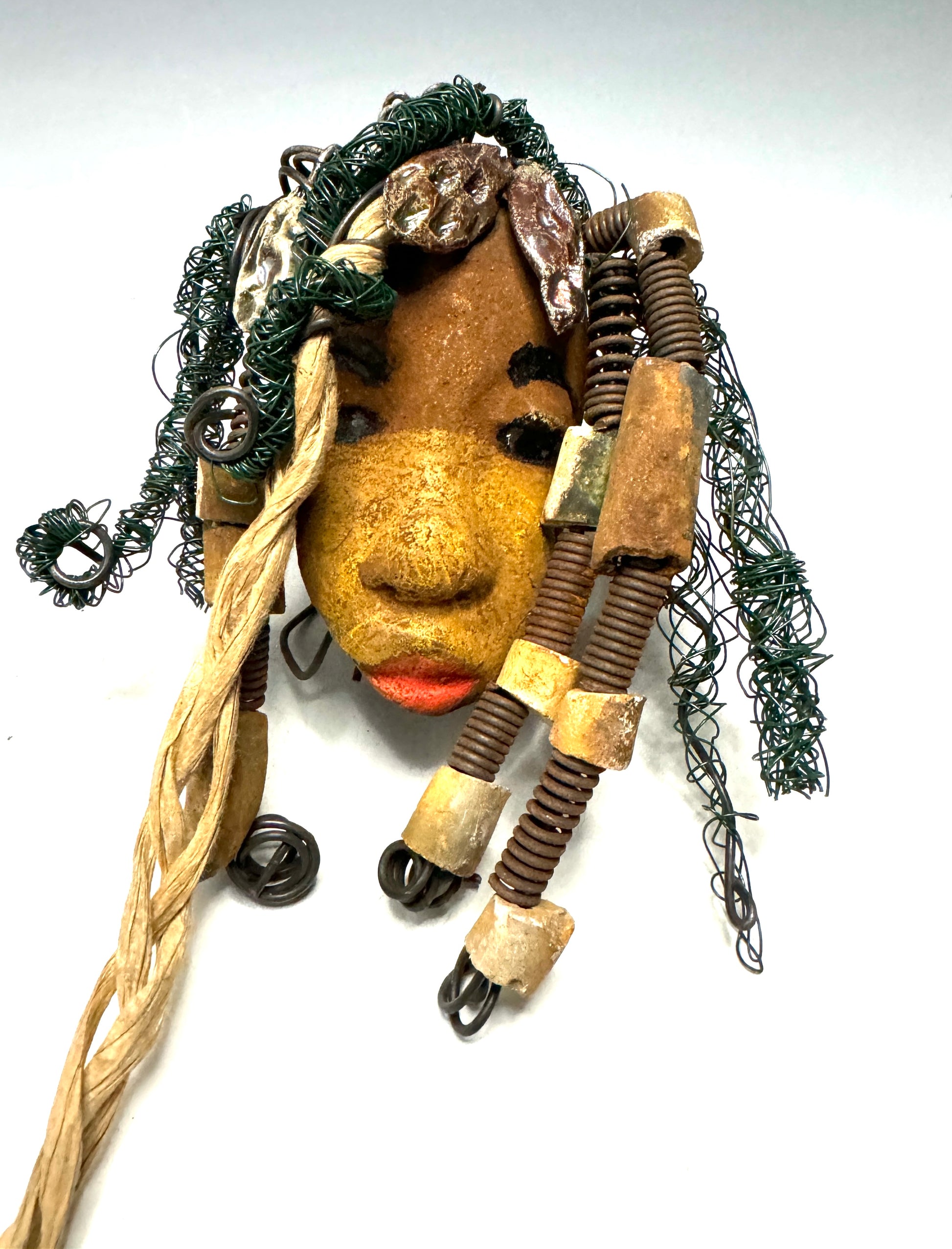 Wanda is a 5" x 8" Raku-fired mask, featuring 16 and 24-gauge wire over 20ft in length. Her two tone honey brown complexion is the perfect contrast to her green-coiled locs. Get her this holiday season at a discount, making it the perfect time to start a collection or gift her as a special surprise.