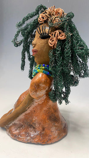 Carmine measures 9" x 6" x 5.5" and weighs 2 lbs, with honey brown complexion and reddish brown lips. Her long hair boasts copper strands and over 80 feet of 24 and 16 gauge twisted wire, reaching her waist. She has vibrant metallic copper red antique glazed eyes that impart a feeling of hope, and her charming presence will always initiate conversations