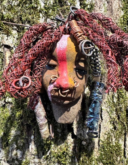 Billy is a 5" x 7" Raku-fired mask with intricate detail. Constructed with 16 and 24-gauge wire, spanning a total of 20 feet, he features a two tone, honey brown and red stripe complexion, matched with vibrant red coiled locs. Now available at a discount, Billy is an ideal choice for collectors or as a special holiday surprise.