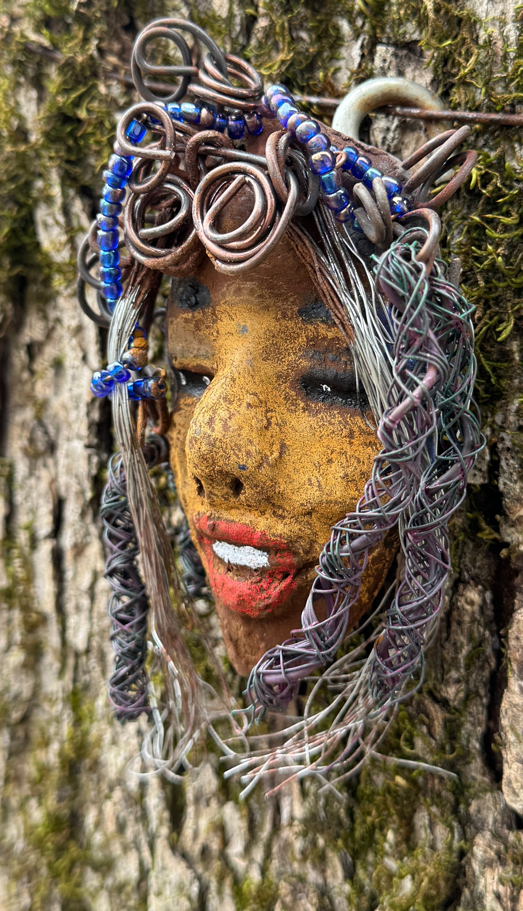 Agnes is a "4 x 6" raku mask displayed in a glass covered black shadowbox, accented with a beautiful two-tone honey brown complexion. Her intricate hair, made of 16 and 24 gauge wire, measures over 50 feet in length. With a contagious smile, Agnes adds a touch of elegance to any home decor.