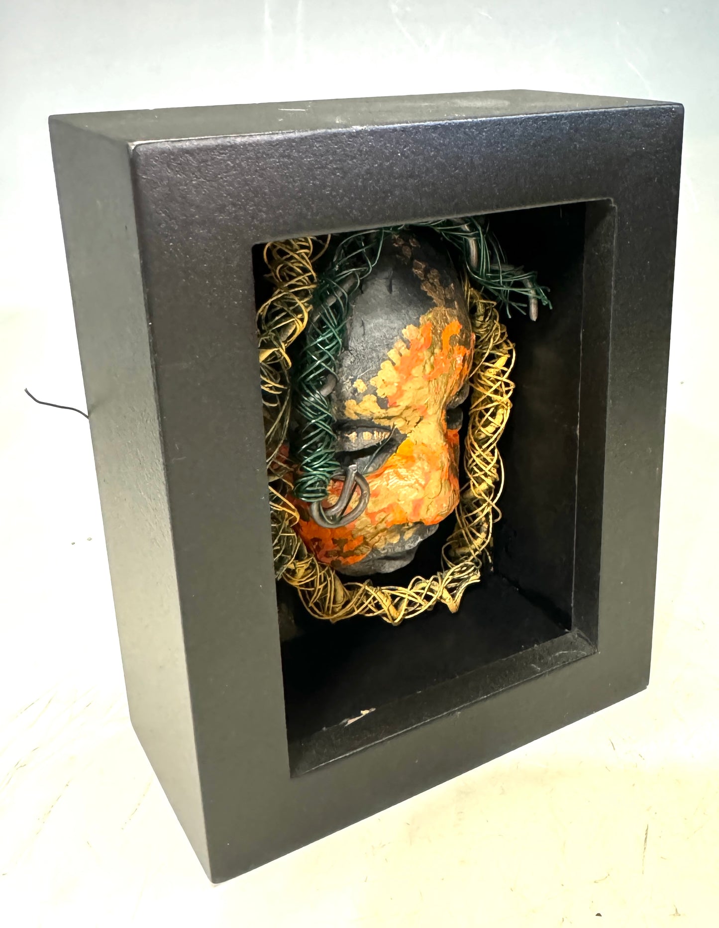 Jake is a mixed media mask that is raku fired and enclosed in a 4“ x 4“ black shadowbox. He has over 25 feet of 16 and 24 gauge wire as hair. 