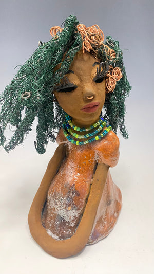 Carmine measures 9" x 6" x 5.5" and weighs 2 lbs, with honey brown complexion and reddish brown lips. Her long hair boasts copper strands and over 80 feet of 24 and 16 gauge twisted wire, reaching her waist. She has vibrant metallic copper red antique glazed eyes that impart a feeling of hope, and her charming presence will always initiate conversations