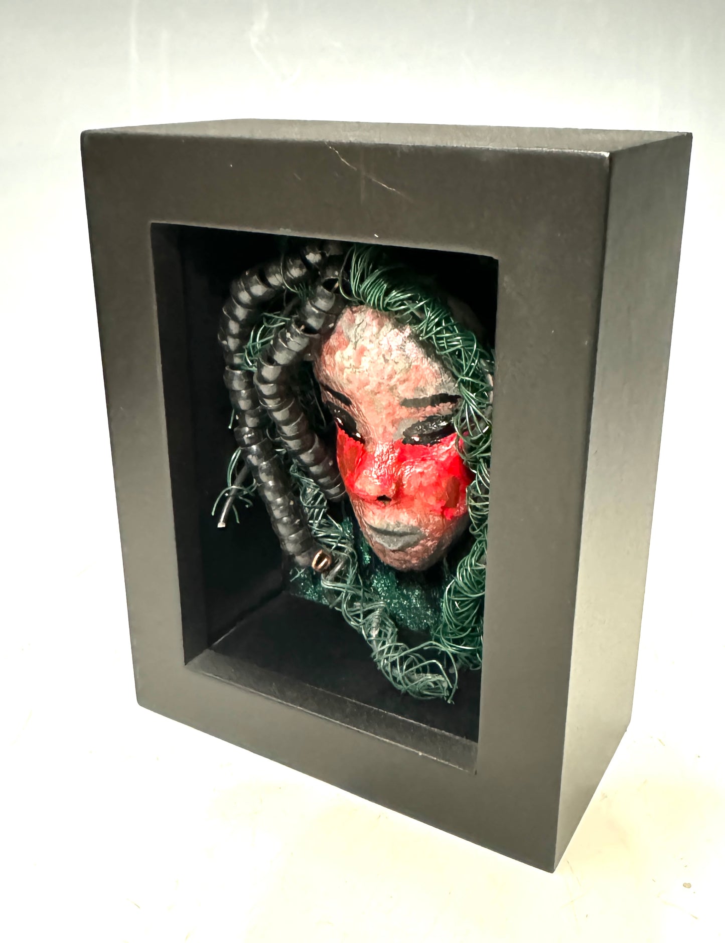 Adia is a striking mixed media mask, raku fired and displayed in a sleek black shadowbox. With over 25 feet of wire for his hair, this unique piece adds an adventurous touch to any space and showcases your bold style. Don't settle for ordinary - stand out with Adia.