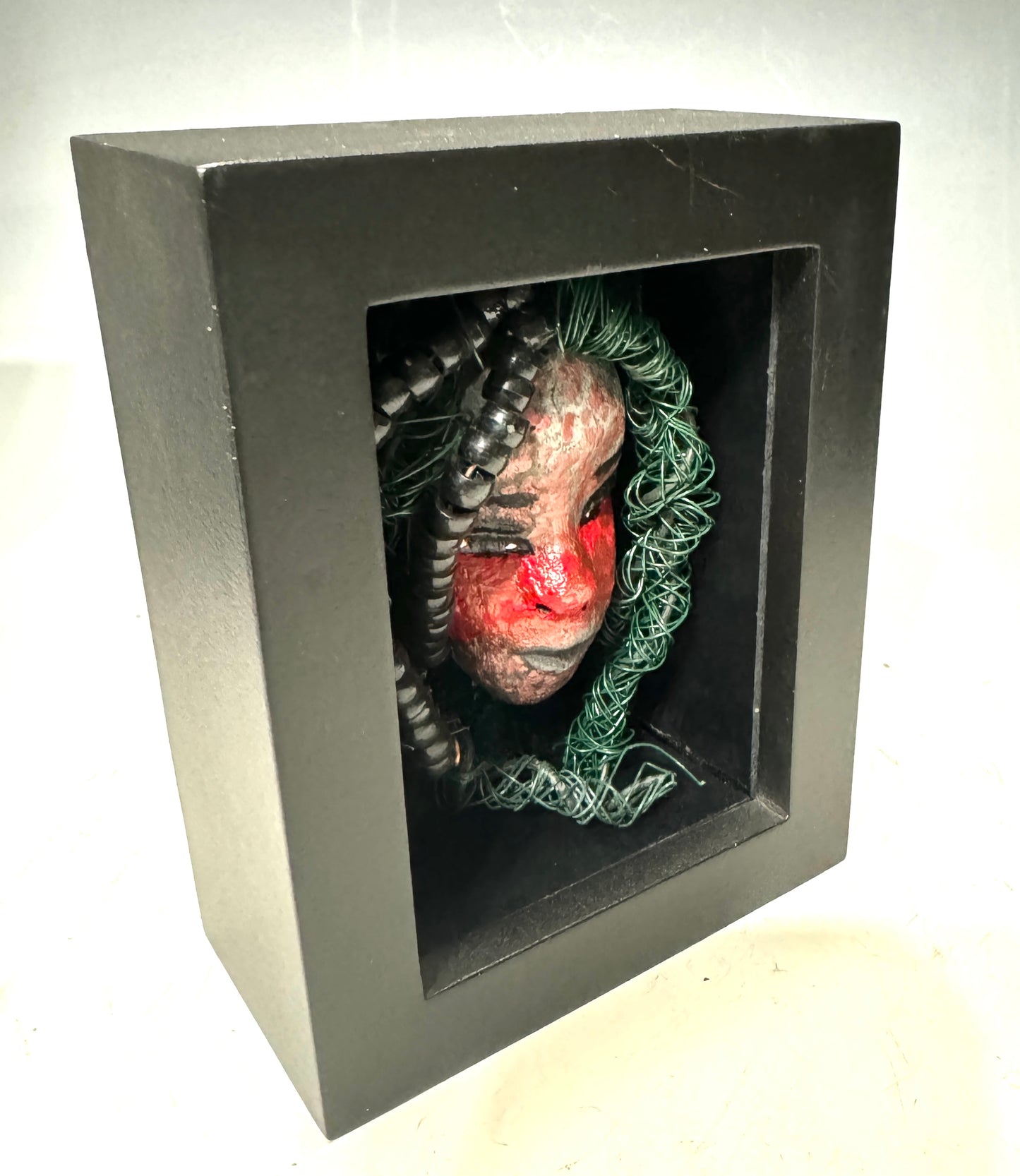 Adia is a striking mixed media mask, raku fired and displayed in a sleek black shadowbox. With over 25 feet of wire for his hair, this unique piece adds an adventurous touch to any space and showcases your bold style. Don't settle for ordinary - stand out with Adia.