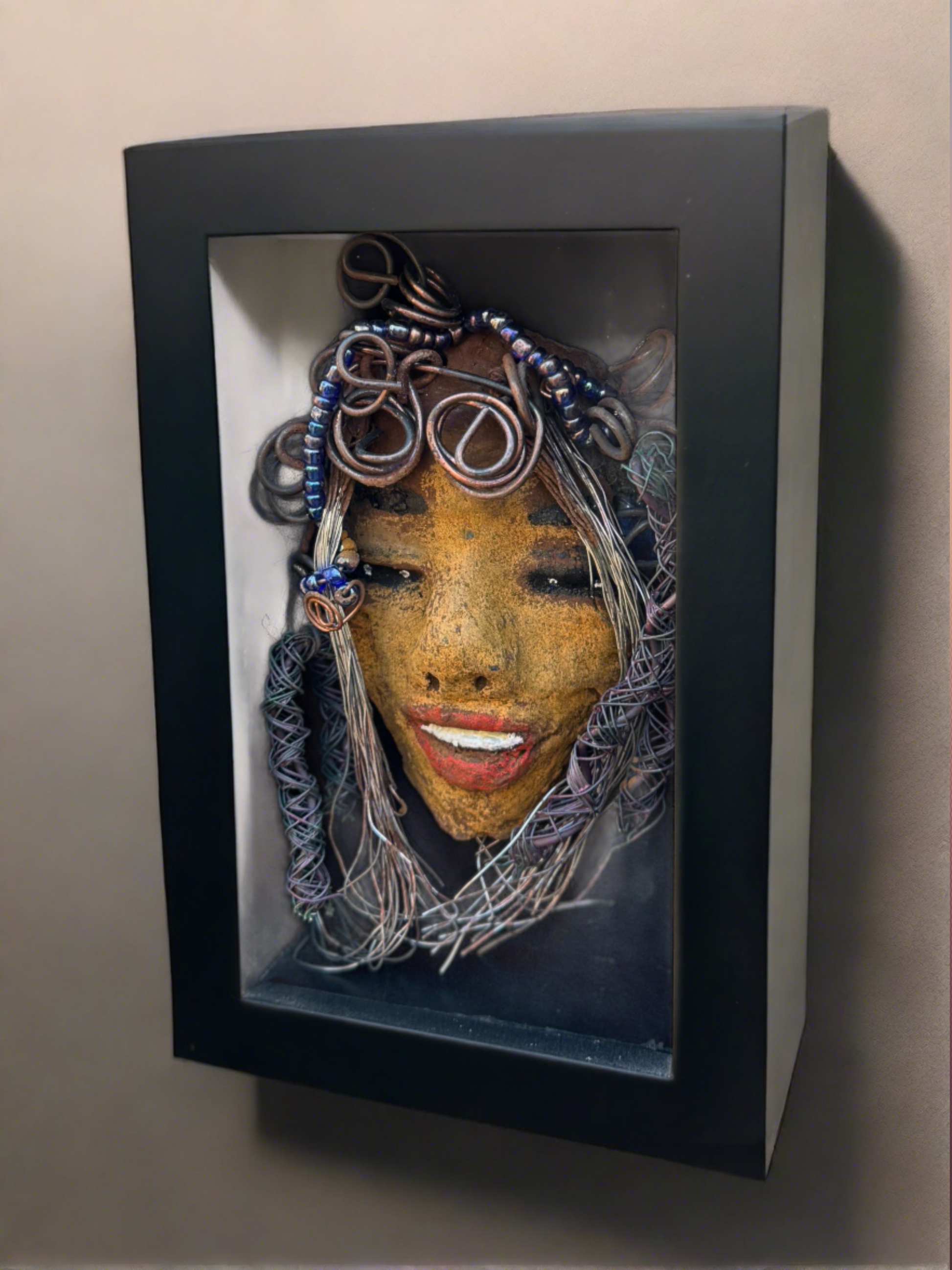 Agnes is a "4 x 6" raku mask displayed in a glass covered black shadowbox, accented with a beautiful two-tone honey brown complexion. Her intricate hair, made of 16 and 24 gauge wire, measures over 50 feet in length. With a contagious smile, Agnes adds a touch of elegance to any home decor.