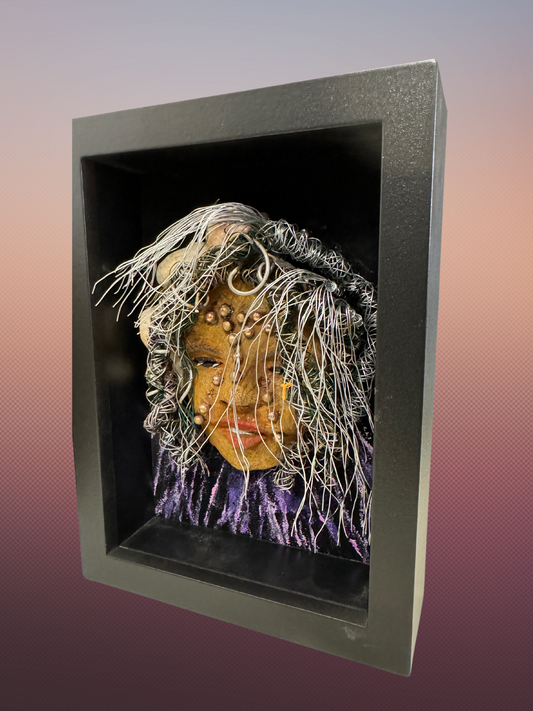 Monika is a "5x 7" raku mask displayed in a glass covered black shadowbox, accented with a beautiful two-tone honey brown complexion. Her intricate hair, made of 16 and 24 gauge wire, measures over 50 feet in length. With a contagious smile, Monika adds a touch of elegance to any home decor.