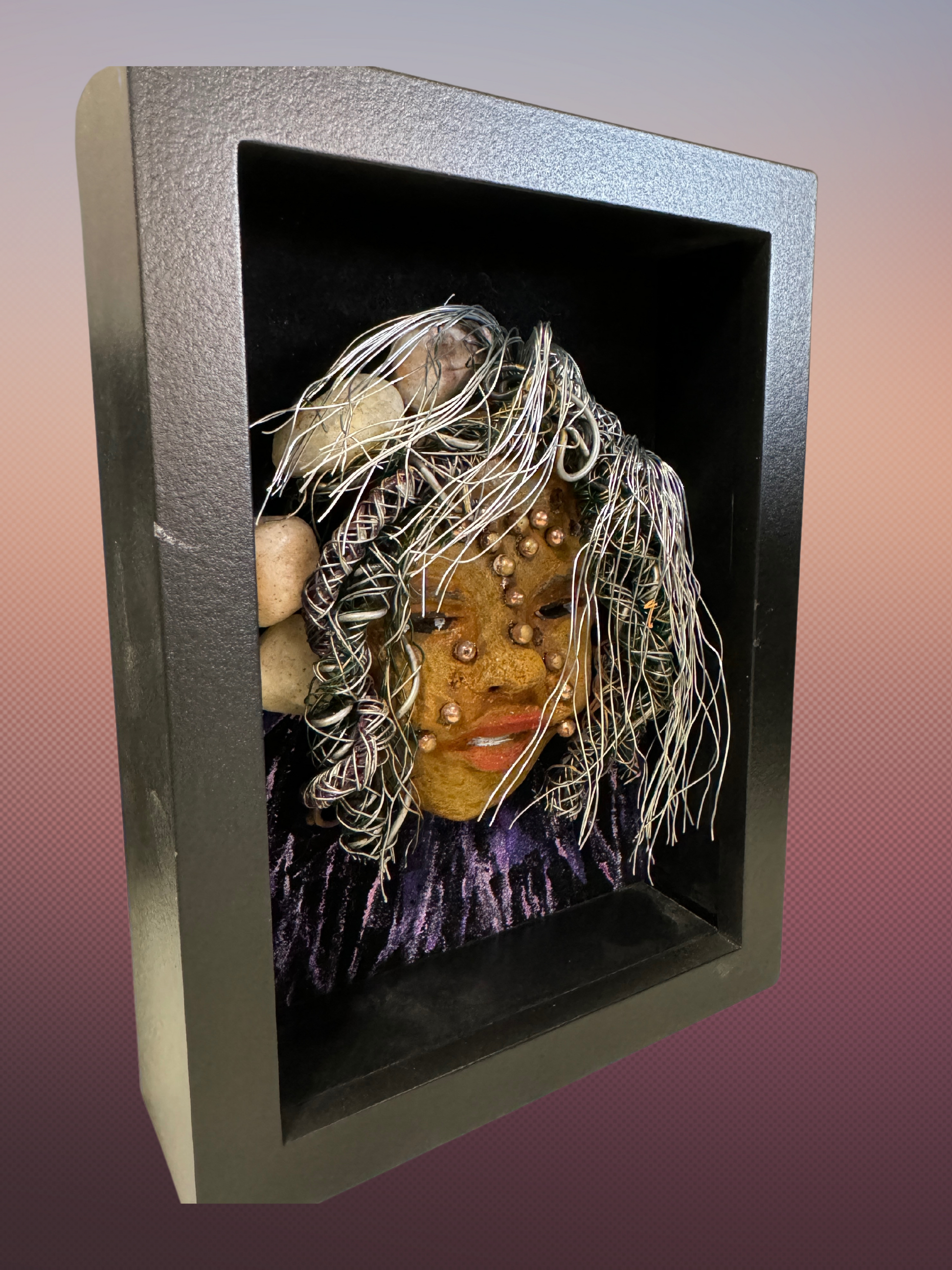 Monika is a "5x 7" raku mask displayed in a glass covered black shadowbox, accented with a beautiful two-tone honey brown complexion. Her intricate hair, made of 16 and 24 gauge wire, measures over 50 feet in length. With a contagious smile, Monika adds a touch of elegance to any home decor.